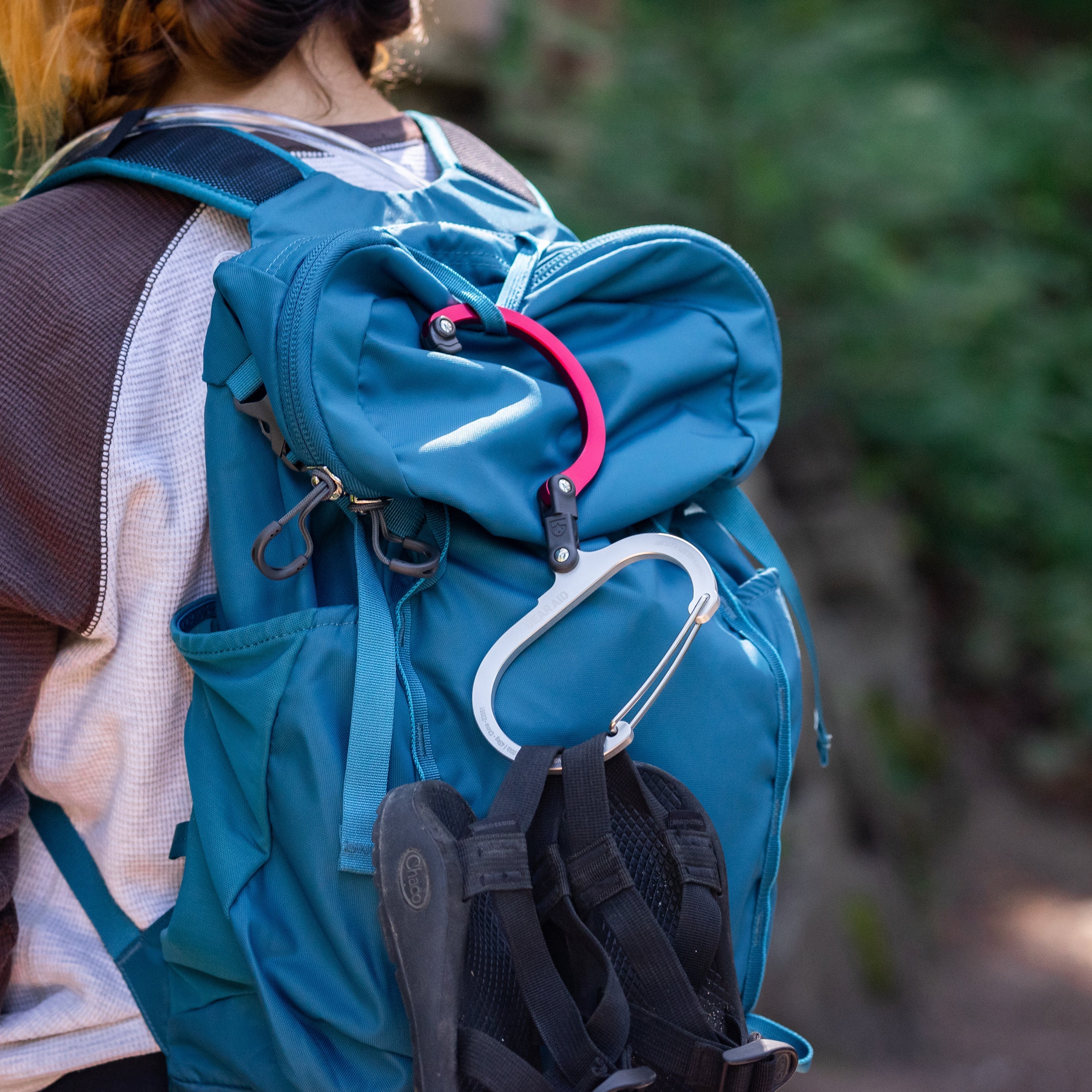 Heroclip open and hanging on a backpack of person hiking. Shoes are hanging from the heroclip.