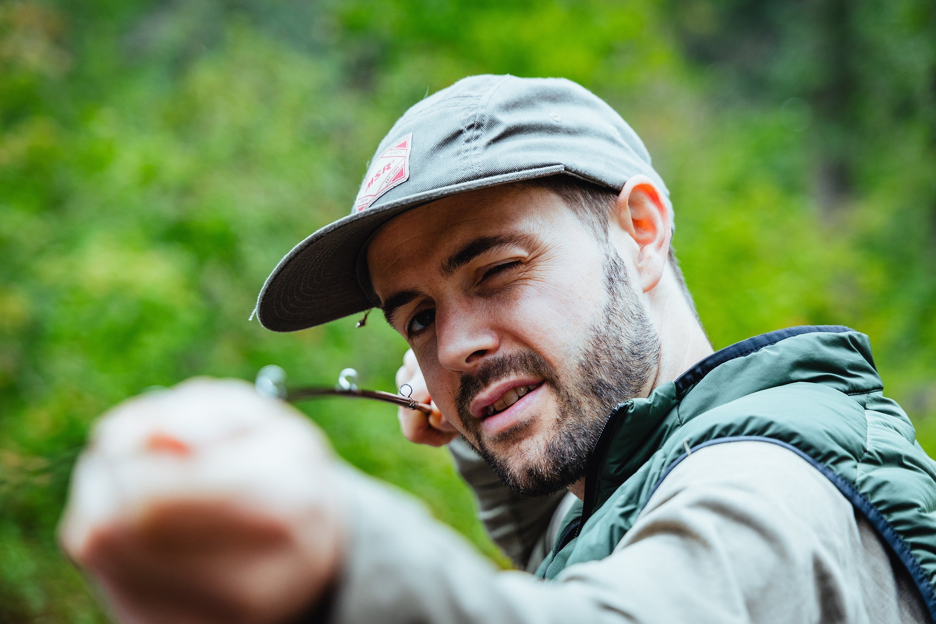 guy measuring fishing rod line in the river with green trees in background