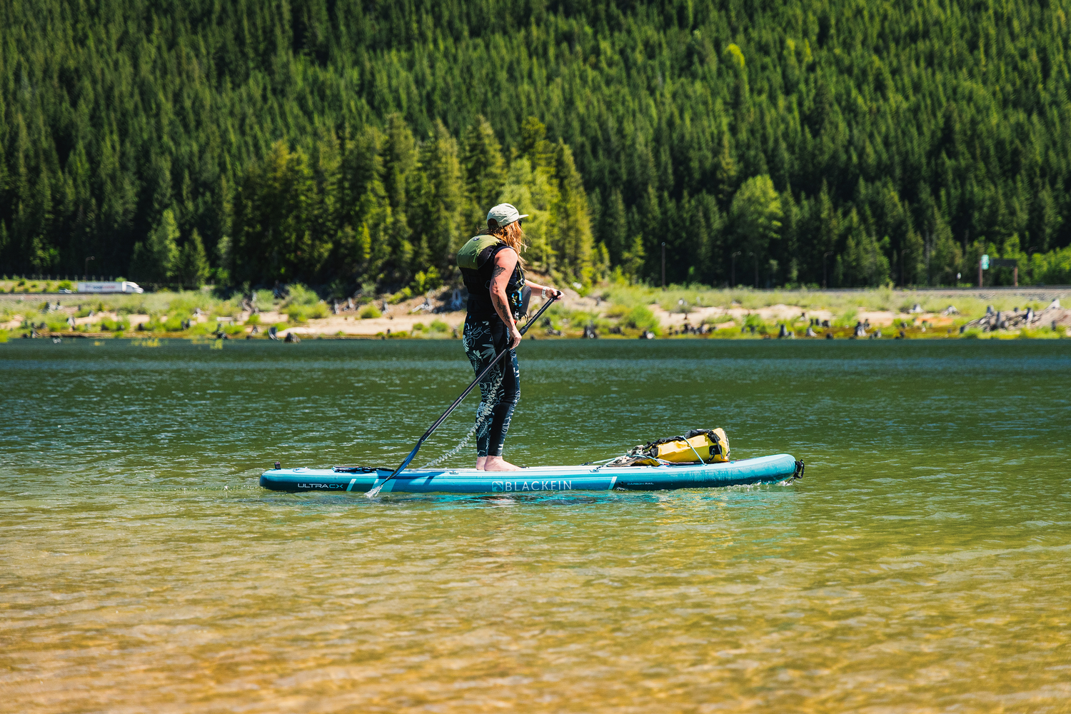 Person on blue paddle board in calm lake with shore and trees in background