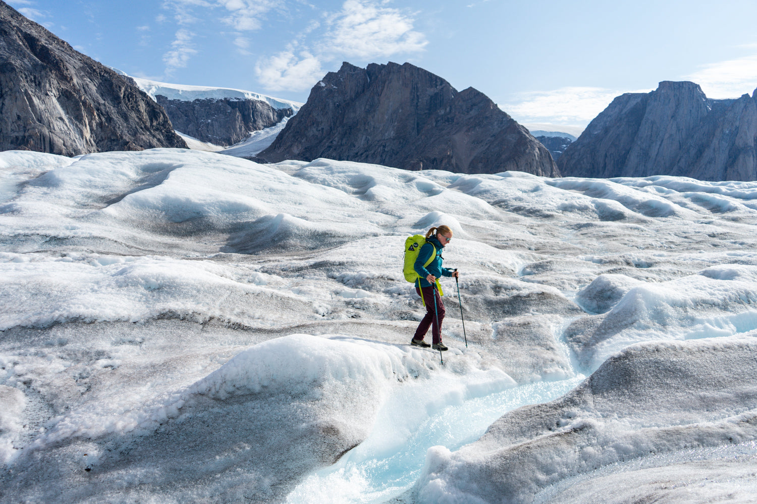 Woman wearing a blue jacket and a bright green pack walking across a glacier in the Arctic