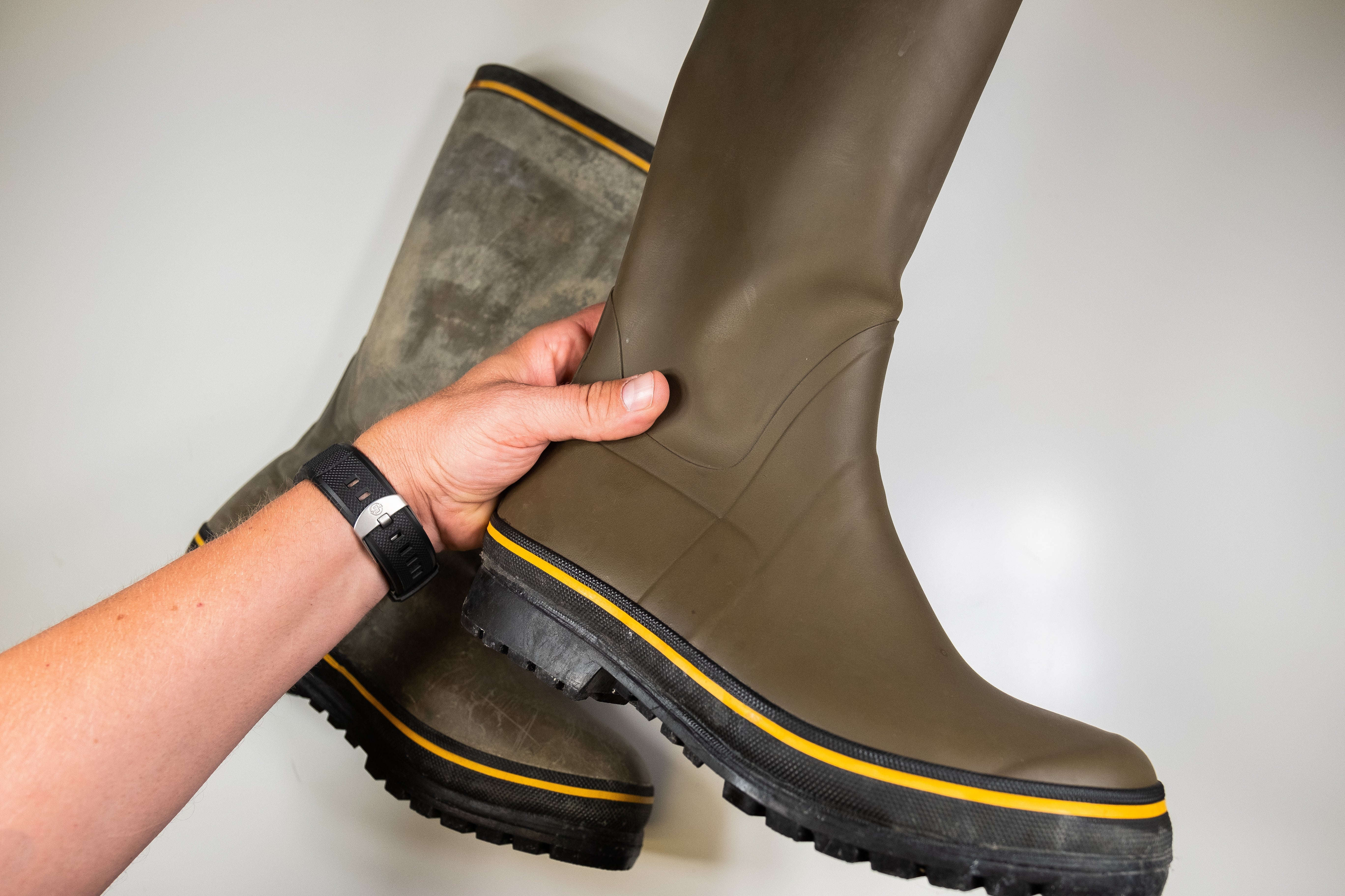 Hand holding up treated rubber boot, untreated boot in the background on a white table