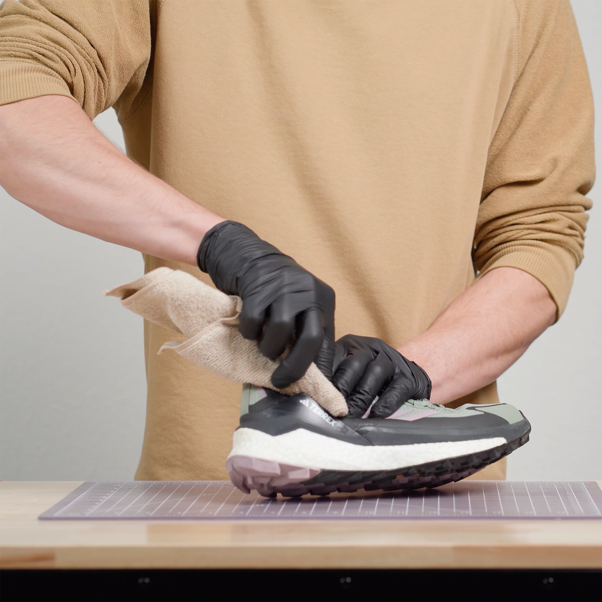 Person wearing black gloves cleaning a damaged trail runner with a cloth