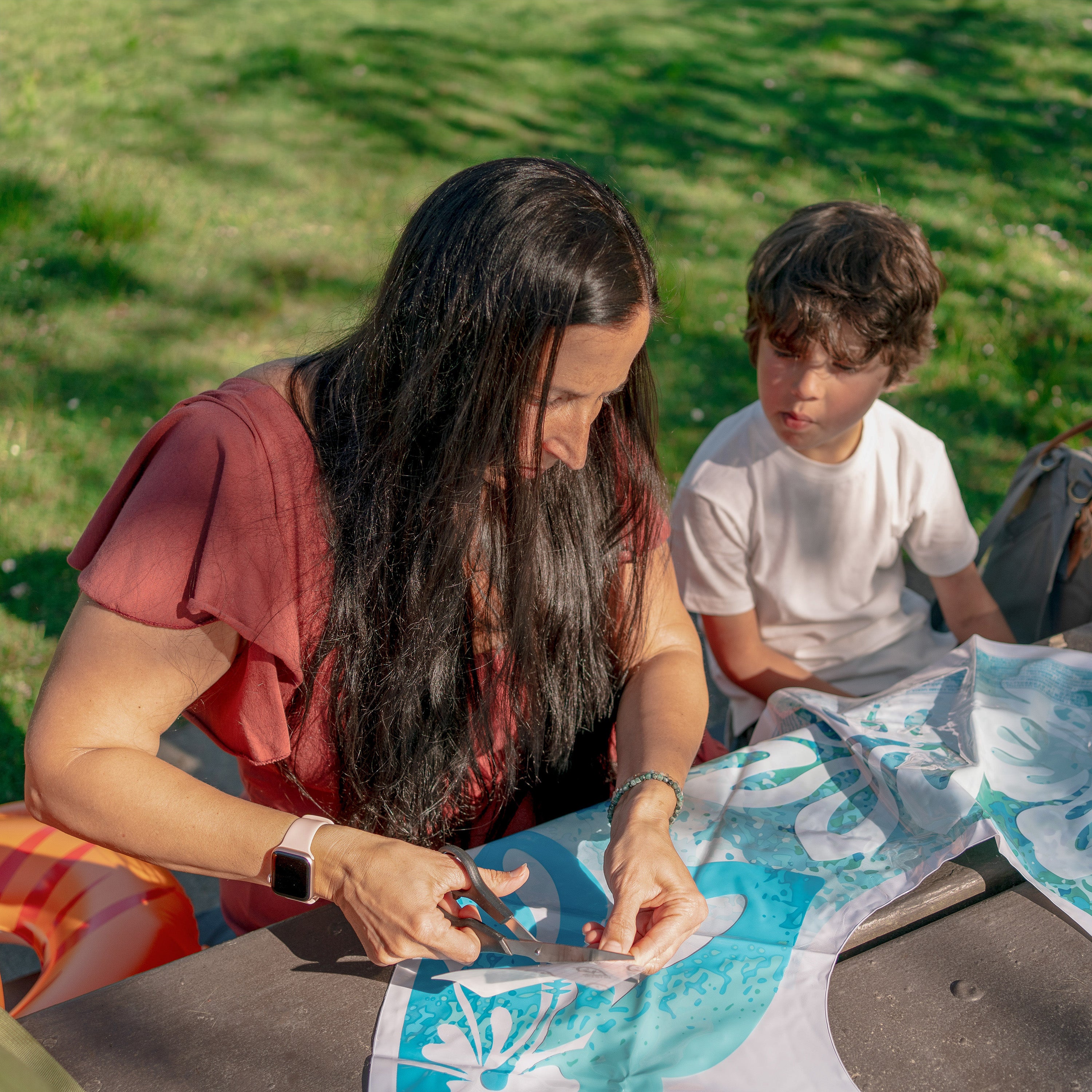 Woman and child outdoors, working on a craft project with fabric and scissors.