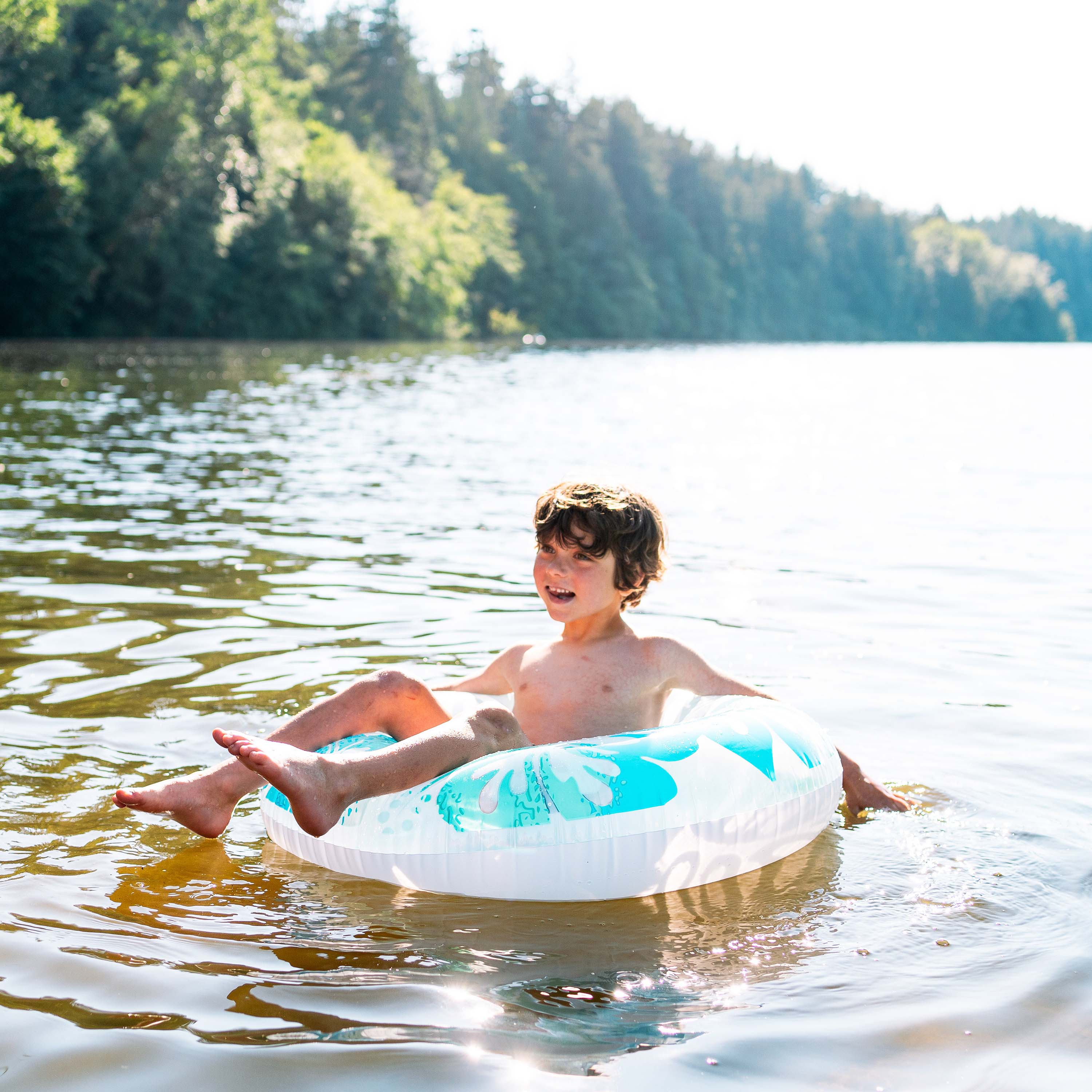 Child on a inflatable ring in a lake with trees in the background