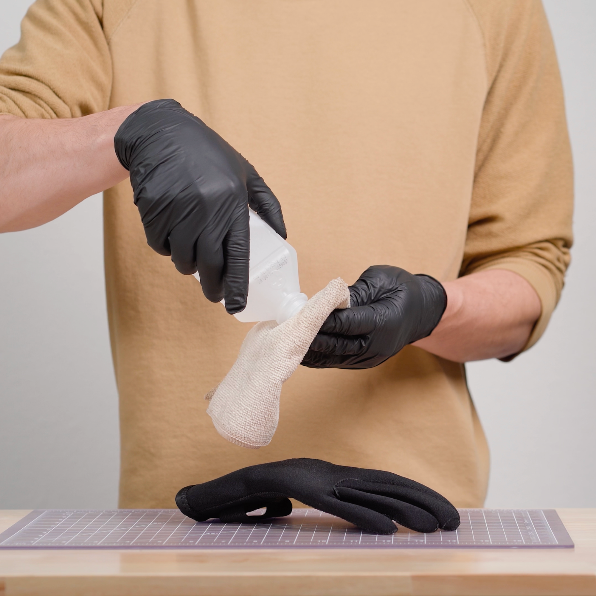 Person wearing black gloves using a cloth and isopropyl alcohol to clean a tear on a neoprene glove