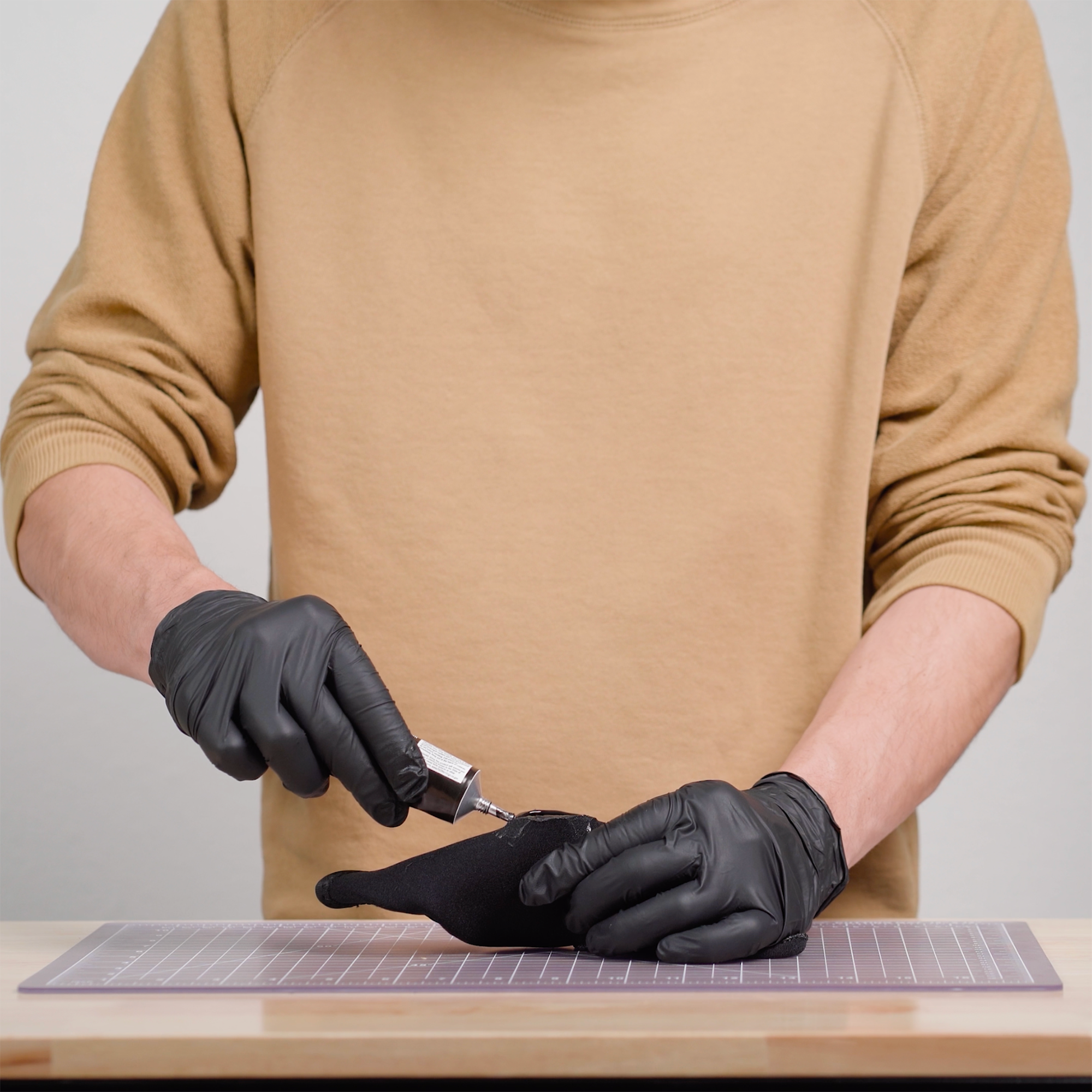 Person wearing black gloves squeezing a small amount of Aquaseal NEO into a tear on a neoprene glove to repair it