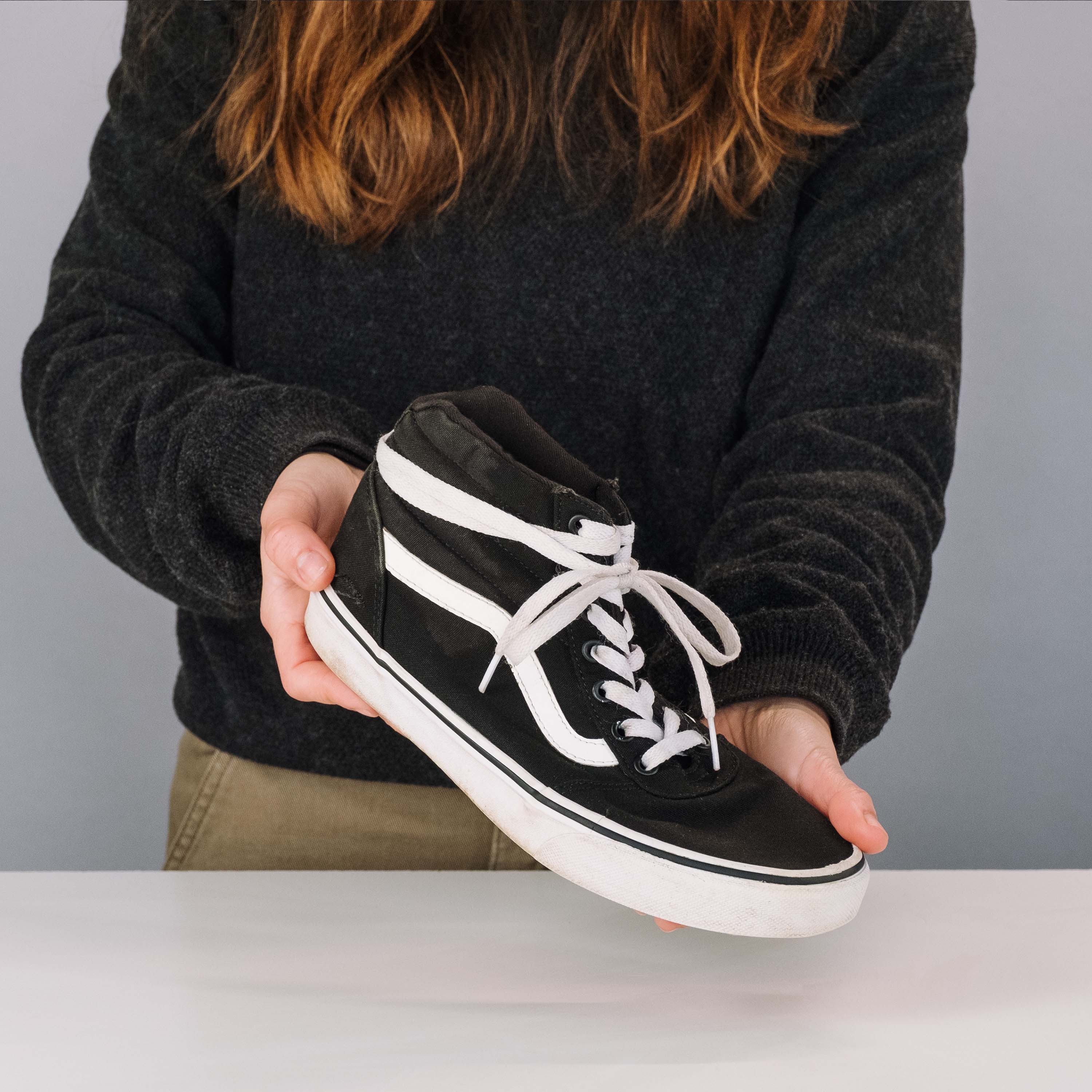 Person holding a black and white sneaker against a neutral background