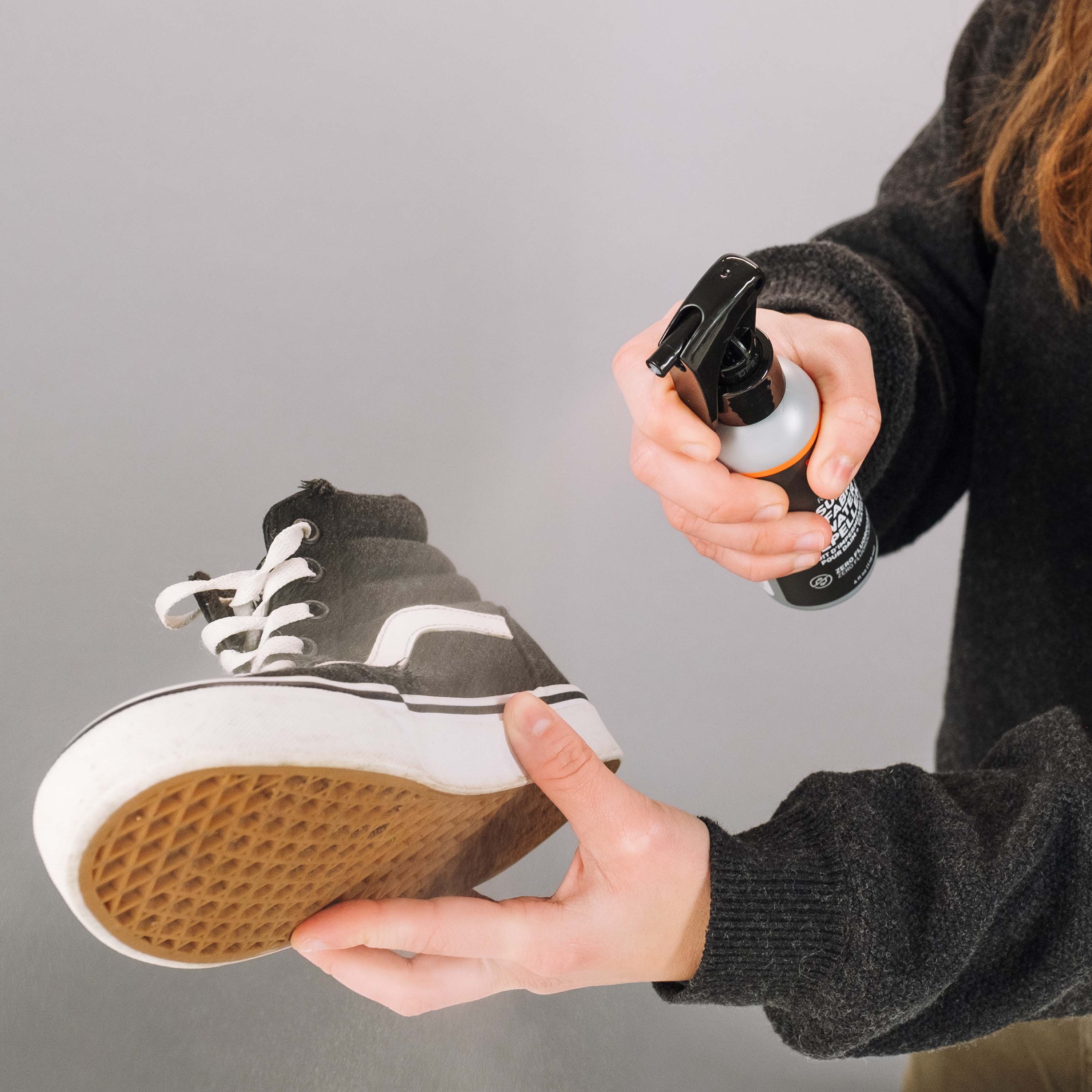 Person holding a sneaker and a spray bottle against a gray background