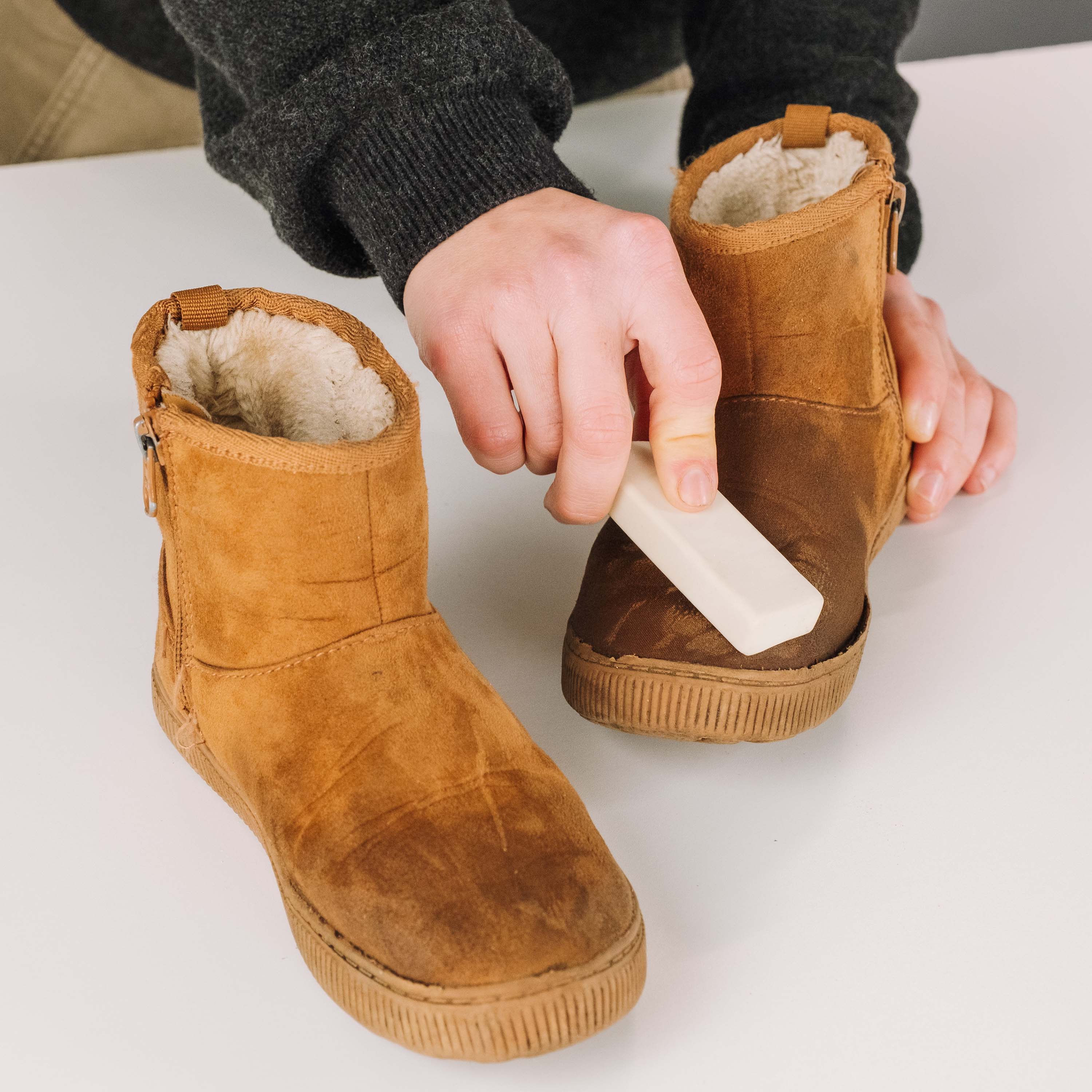 Person applying a white substance to brown suede boots on a light surface