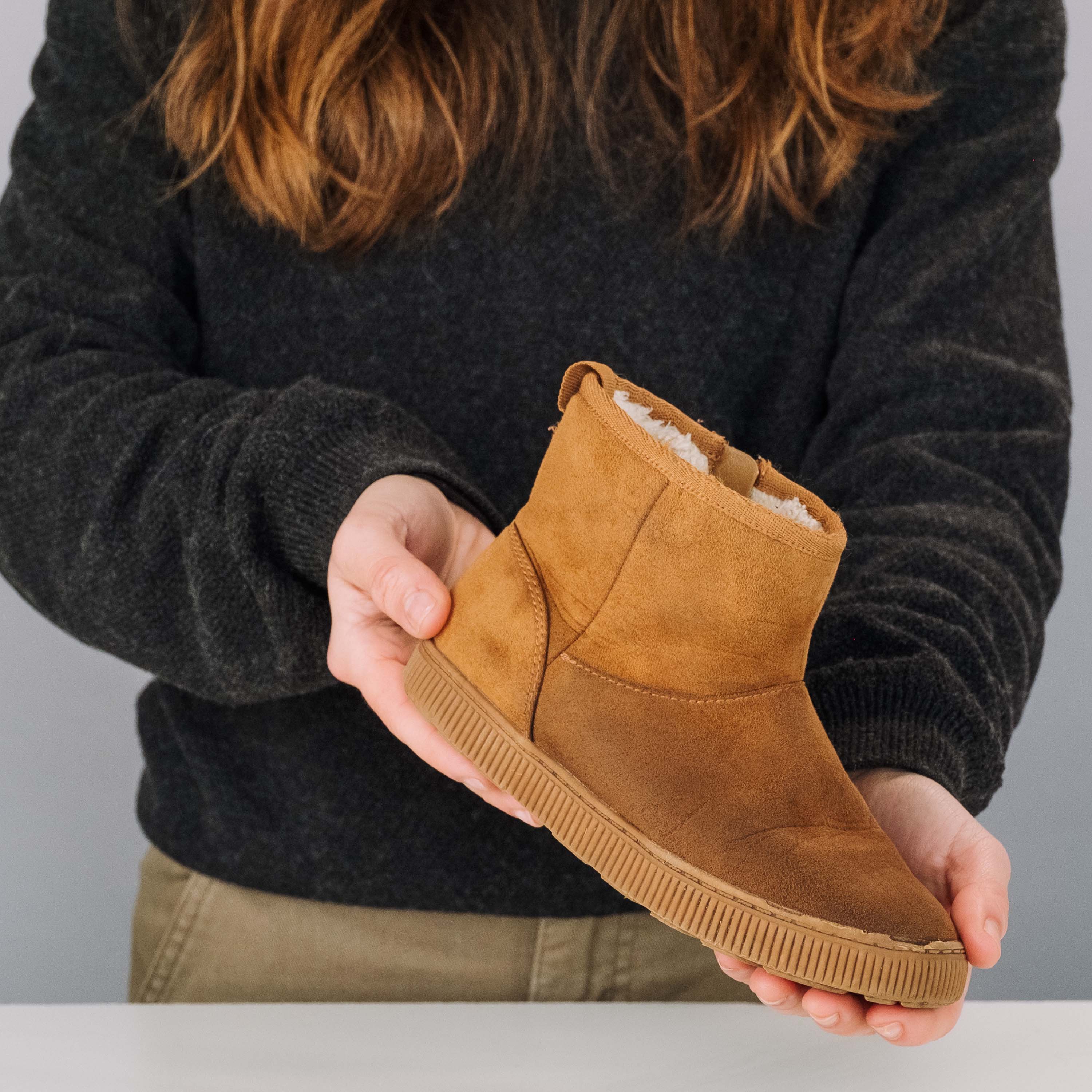 Person holding a brown suede boot with a gray background
