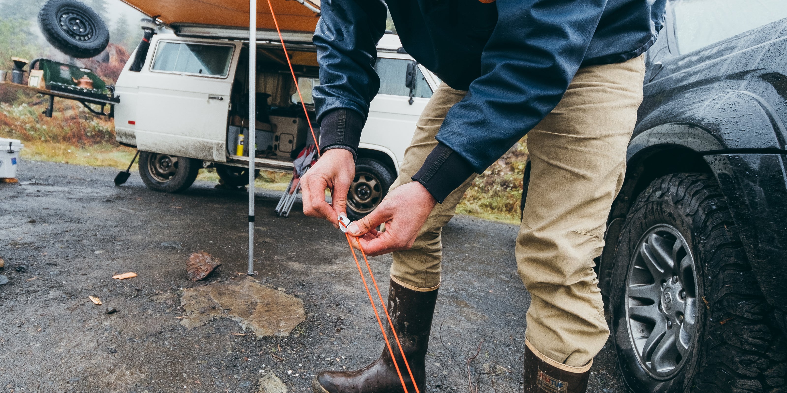 Person setting up a tent with a van and car in the background