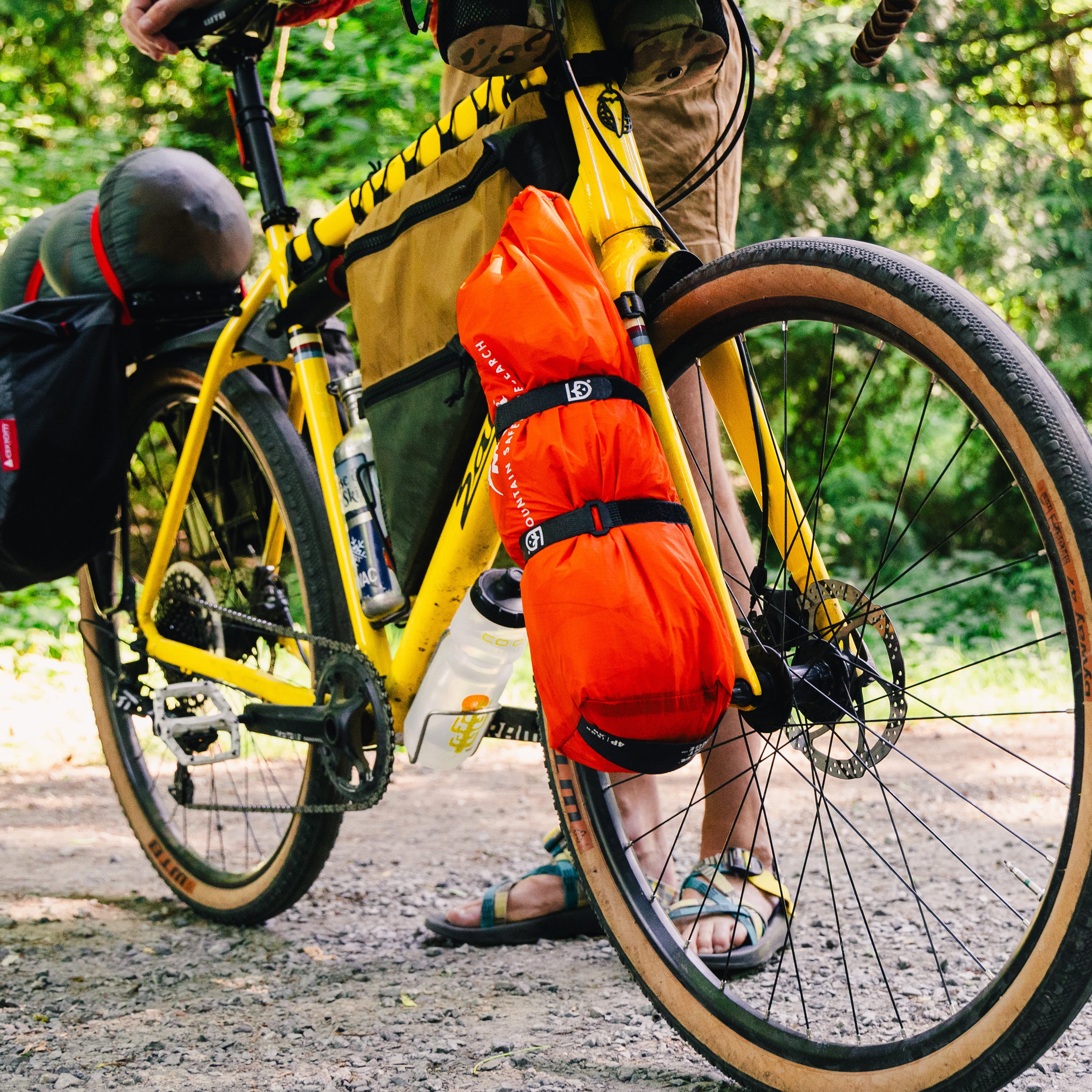 Yellow bicycle with orange bag with Fast Wrap Straps and a person standing next to it on a path.