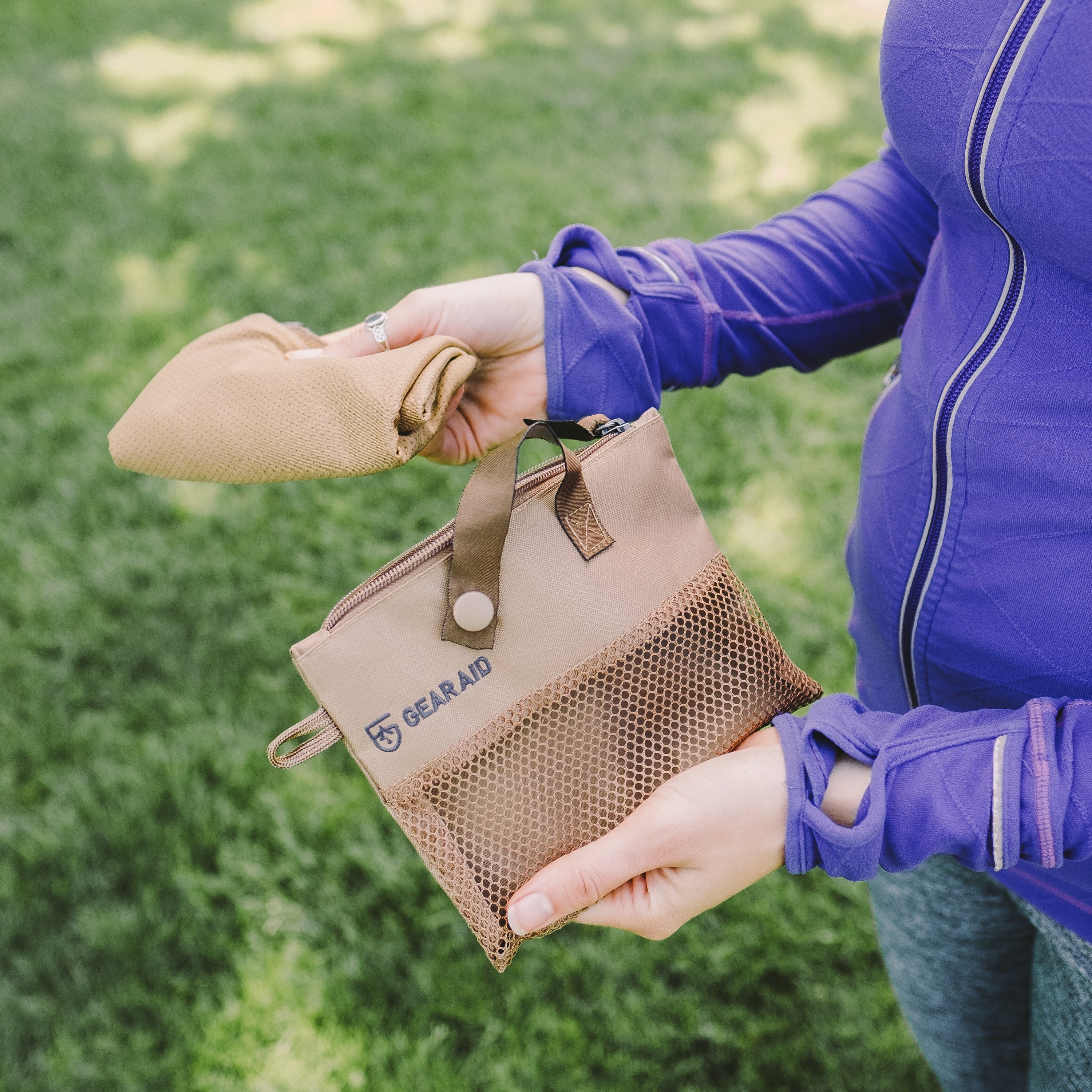 Person holding a beige GEARAID pouch against a grassy background