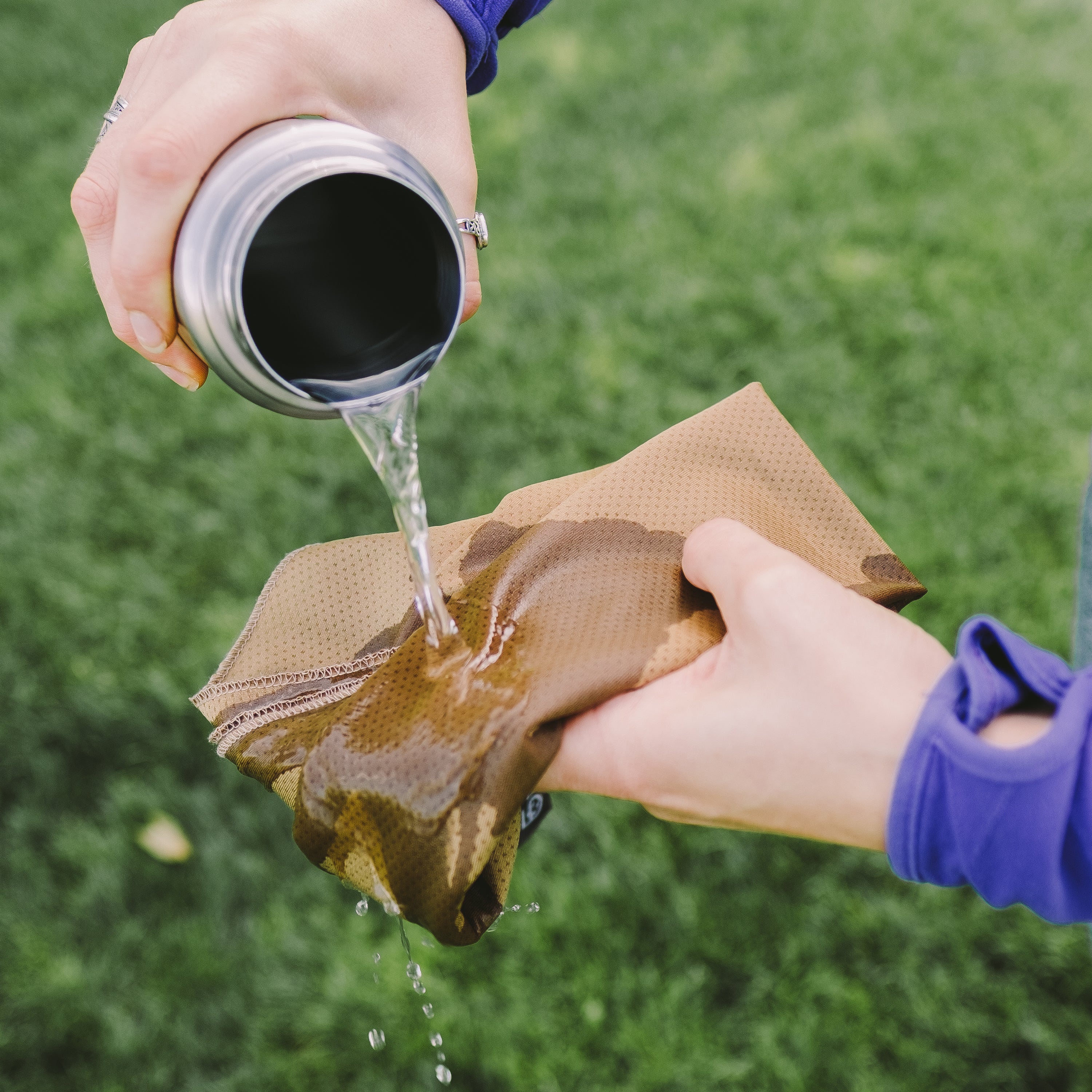 Person pouring water from a thermos onto a brown washcloth held over grass.