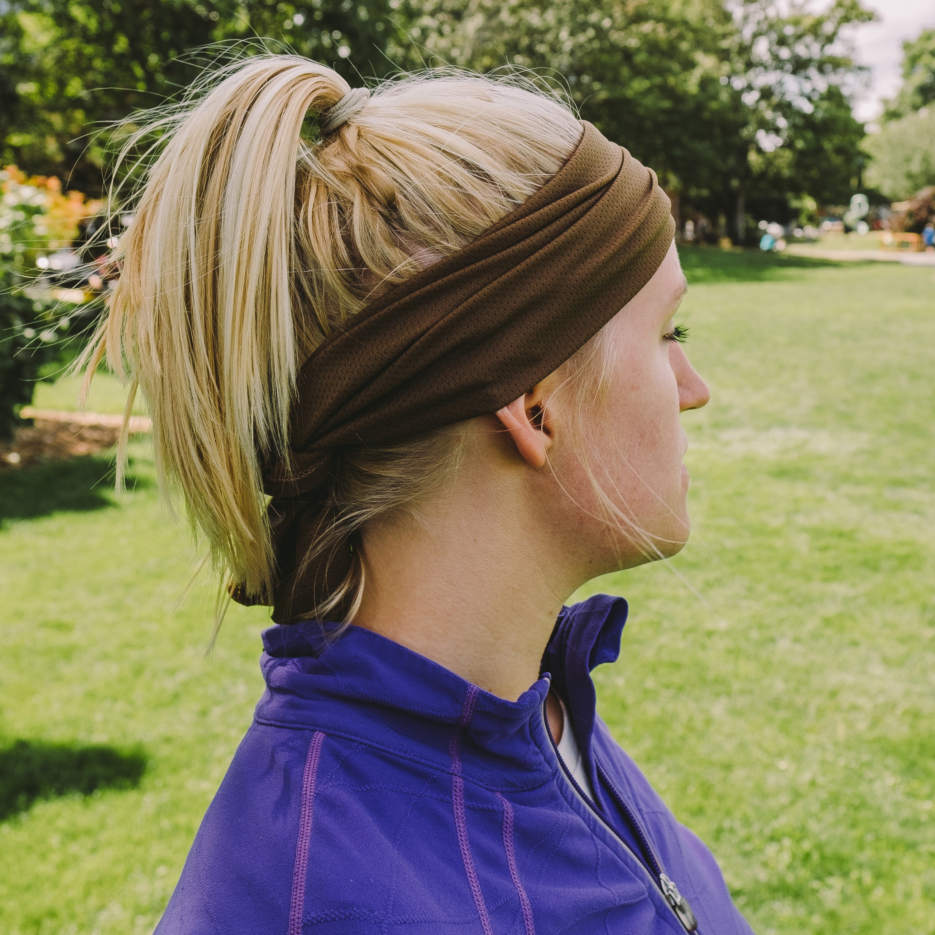 Woman wearing a brown headband and purple jacket in a park.