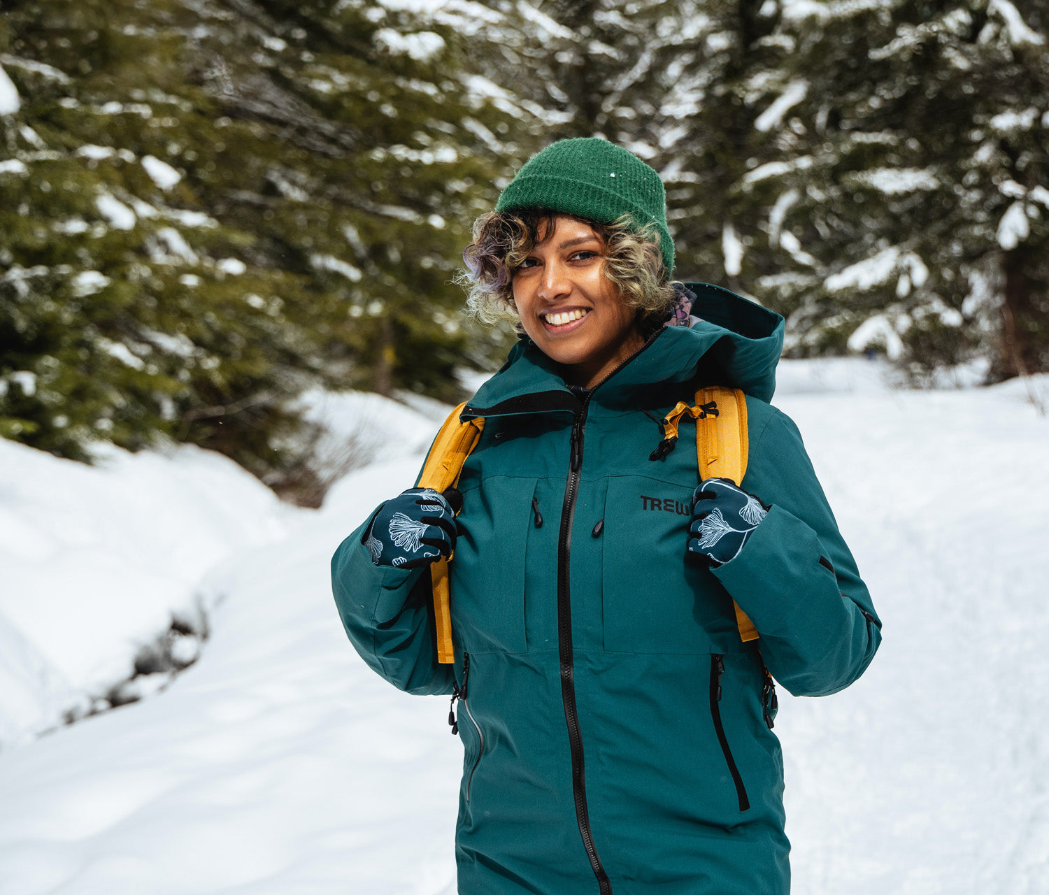 Person wearing a green jacket and hat with a backpack in a snowy forest