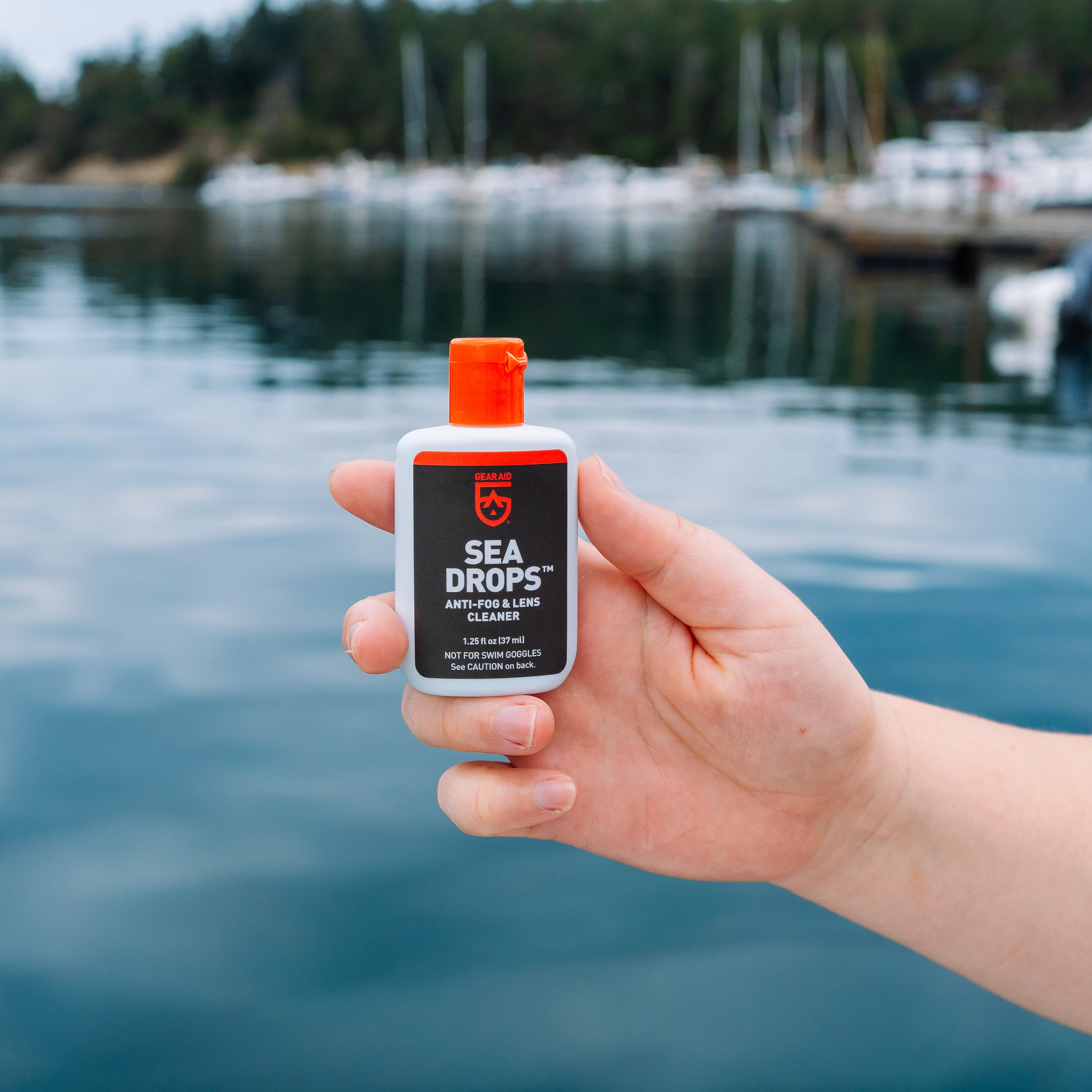 Hand holding a bottle of Sea Drops product with a marina in the background.