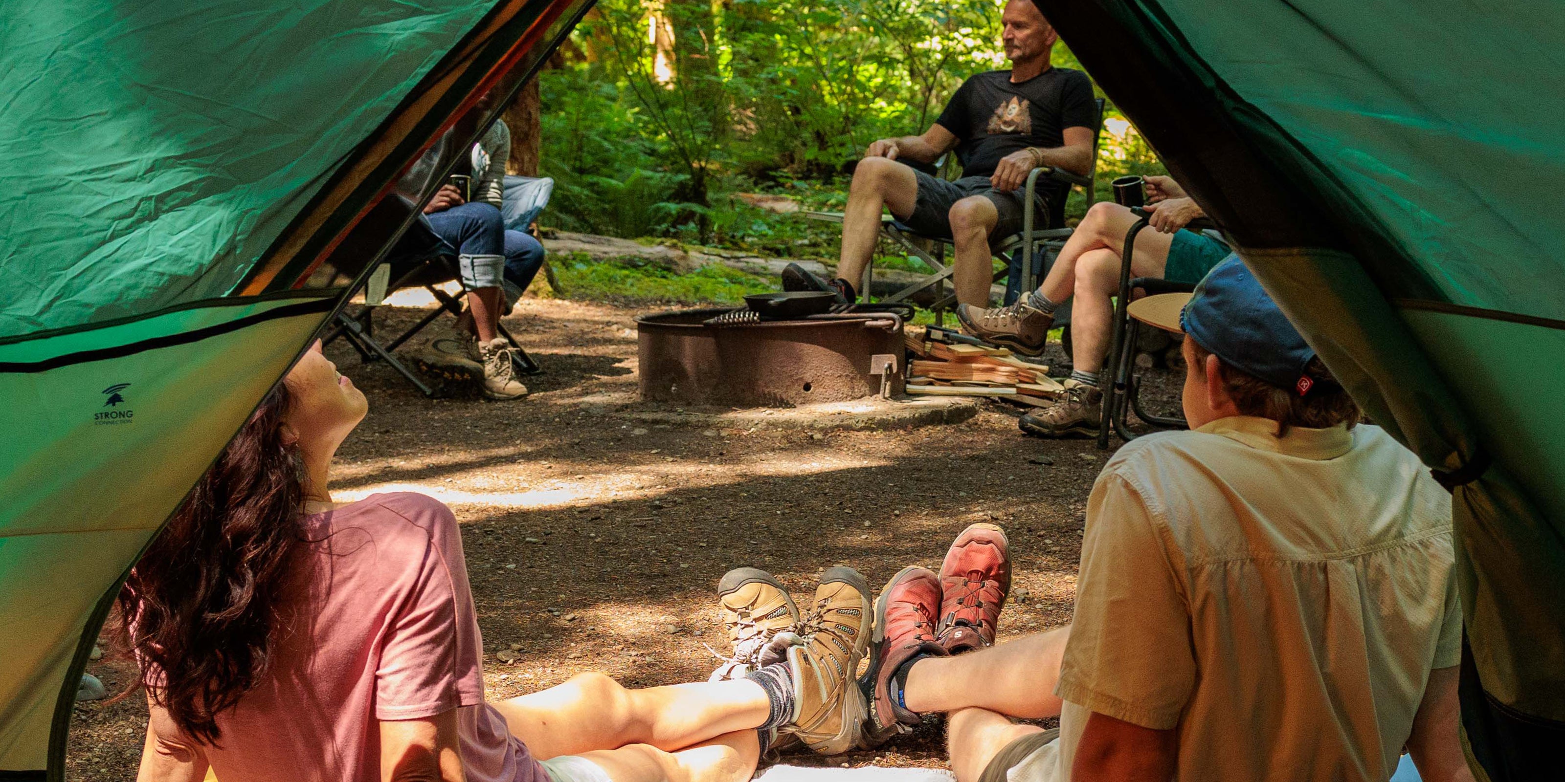 People sitting around a campfire at a campsite with tents and chairs.