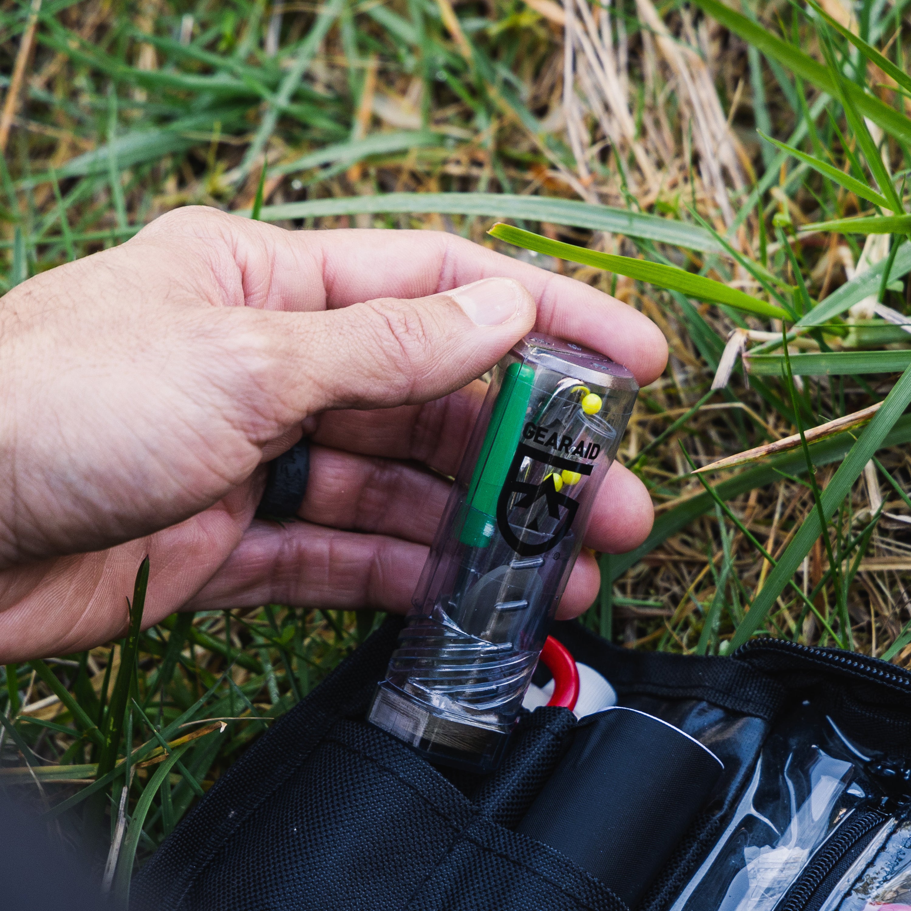 Hand holding a clear container with green and red contents against a grassy background