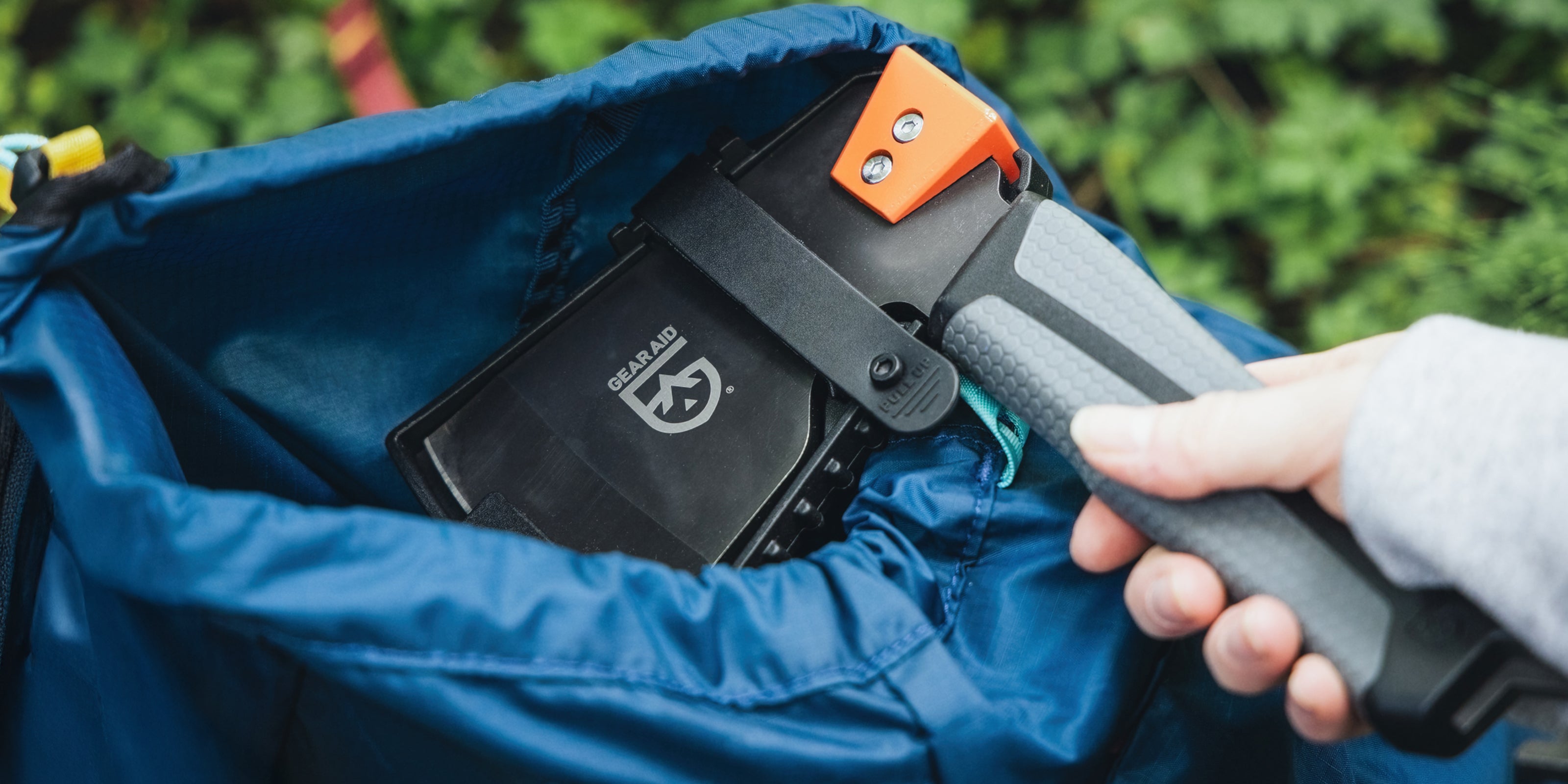 Person using a Balta Camp Hatchet to open a blue bag with a GEAR AID logo.