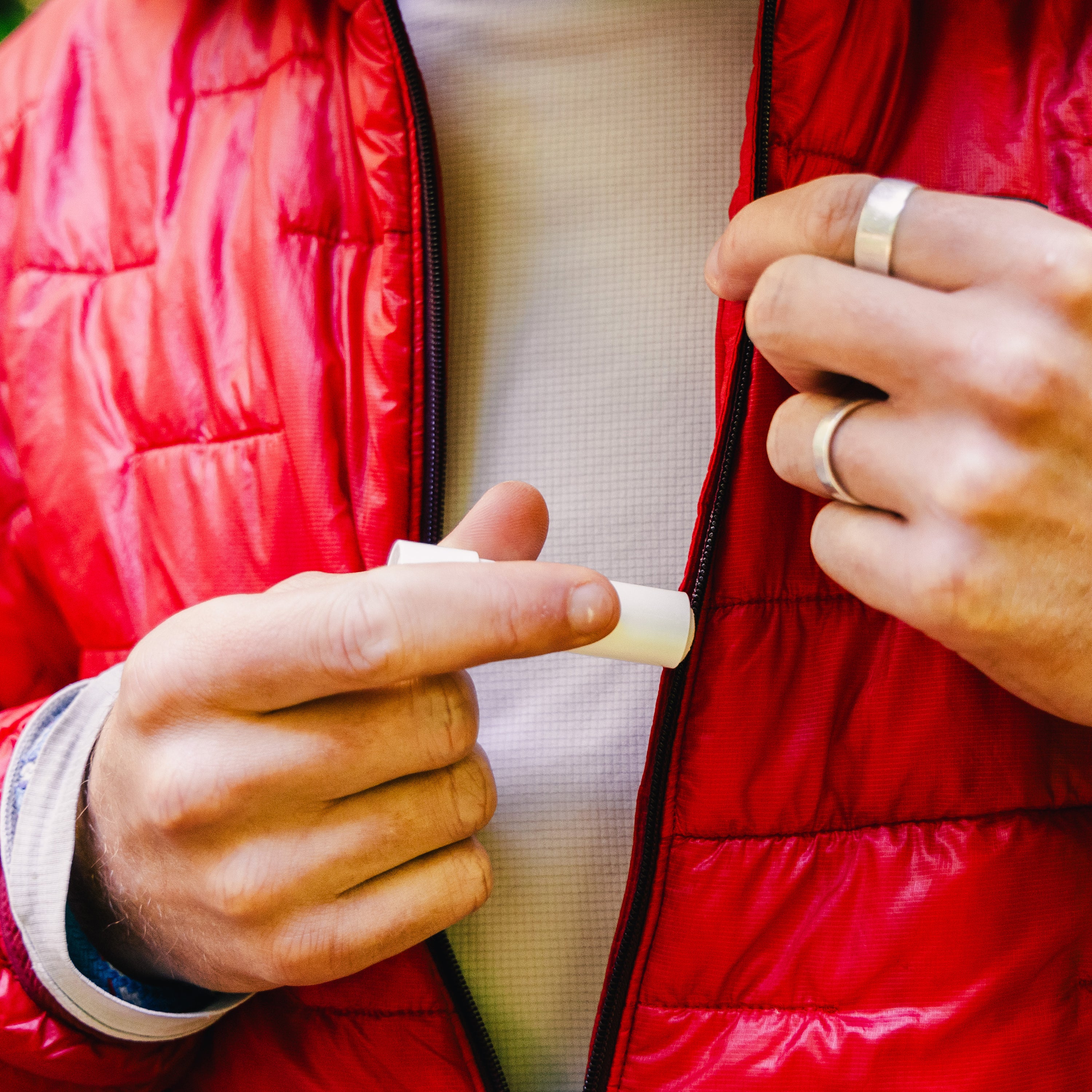 Person in a red jacket applying a small tube of Zipper Lubricant.