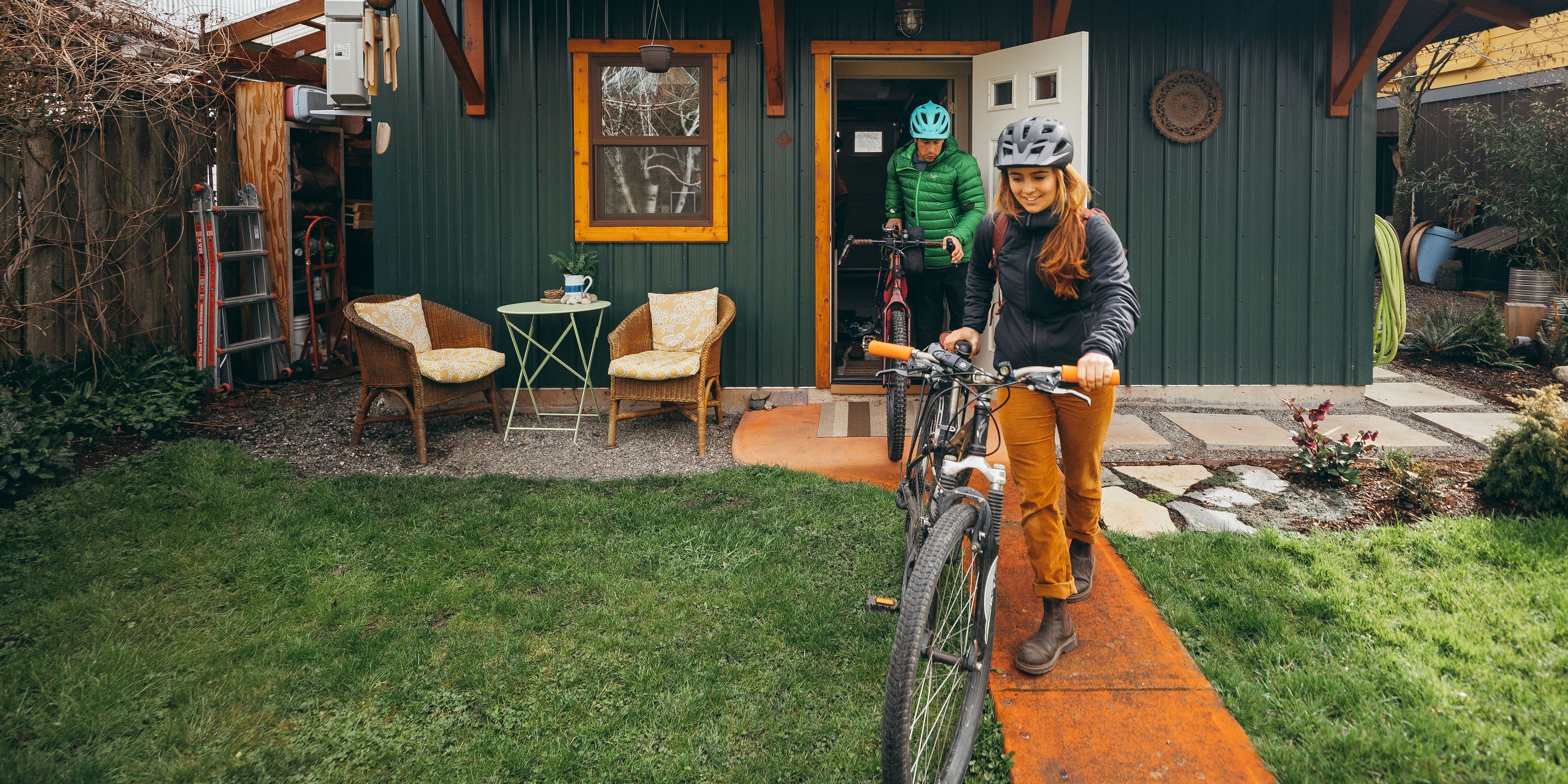 Two people with bicycles in front of a small building with a green exterior.