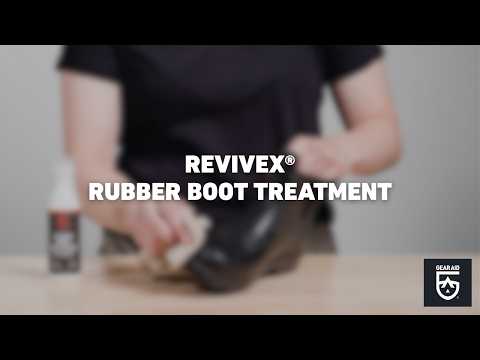 Blurred video cover showing a person applying treatment to a rubber boot with a cloth, with a product bottle on a tabletop nearby, the title “REVIVEX® RUBBER BOOT TREATMENT” centered, and the Gear Aid logo in the bottom-right corner.