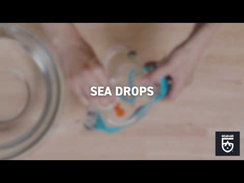 Blurred video cover showing hands holding a snorkel mask on a tabletop, with the title “SEA DROPS” centered and the Gear Aid logo in the bottom-right corner.