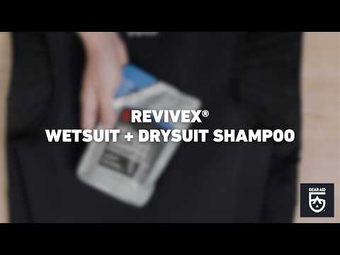 Blurred video cover showing a hand holding a bottle of cleaning solution against a black wetsuit or drysuit, with the title “REVIVEX® WETSUIT + DRYSUIT SHAMPOO” centered and the Gear Aid logo in the bottom-right corner.