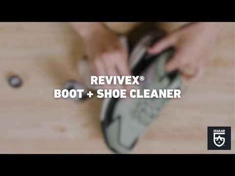 Blurred video cover showing hands cleaning a hiking shoe on a tabletop, with the title “REVIVEX® BOOT + SHOE CLEANER” centered and the Gear Aid logo in the bottom-right corner.