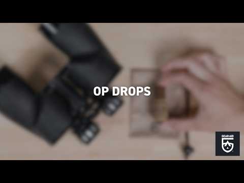 Blurred video cover showing an open product case, a small bottle, and a hand holding a lens, with the title “OP DROPS” centered and the Gear Aid logo in the bottom-right corner.