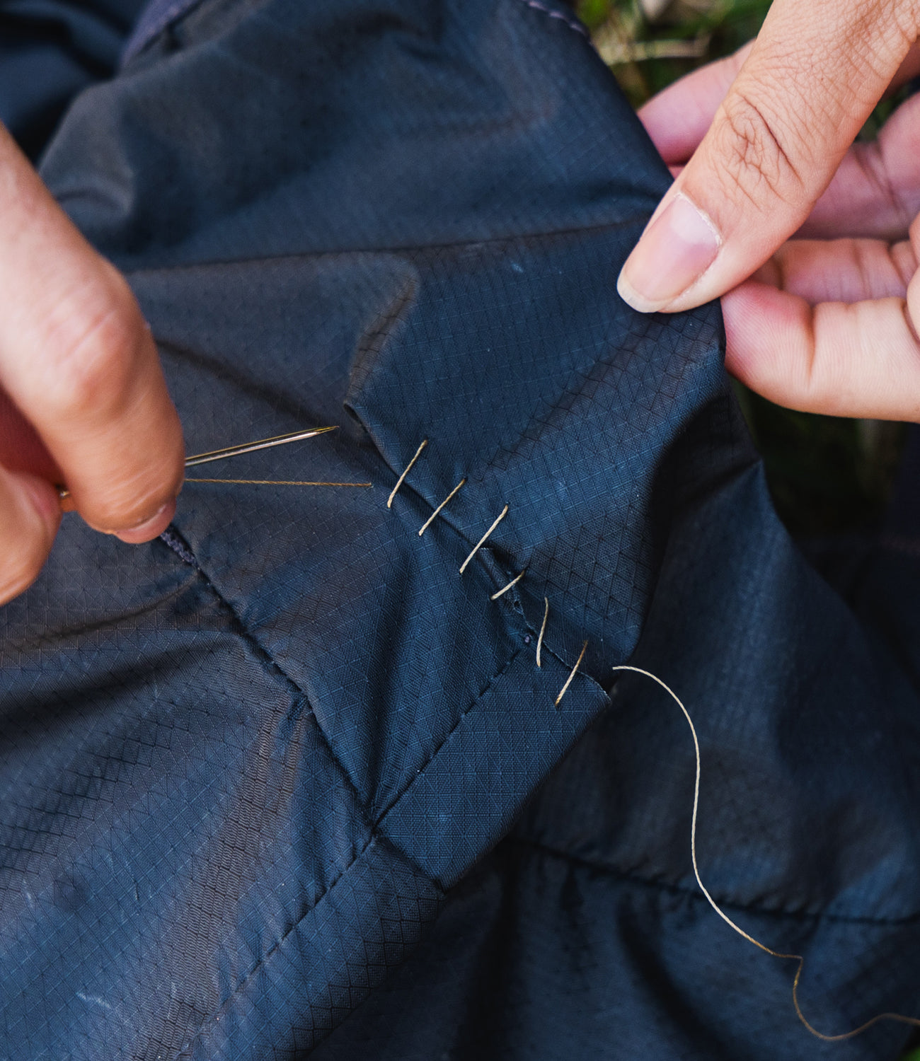 Person sewing blue fabric with a needle and thread