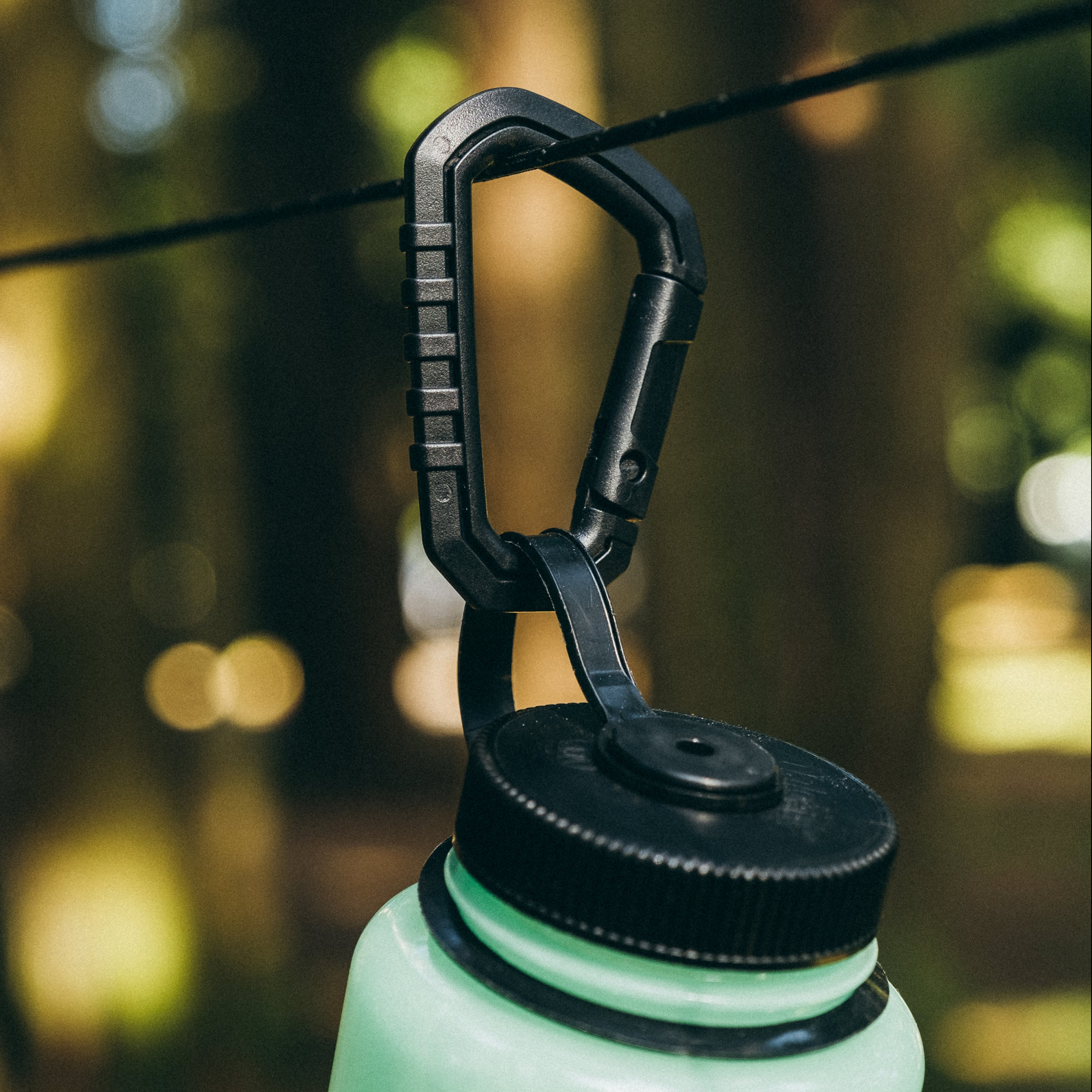 Carabiner that comes included with Fire Strand clipped to a light green Nalgene on a strand of black paracord