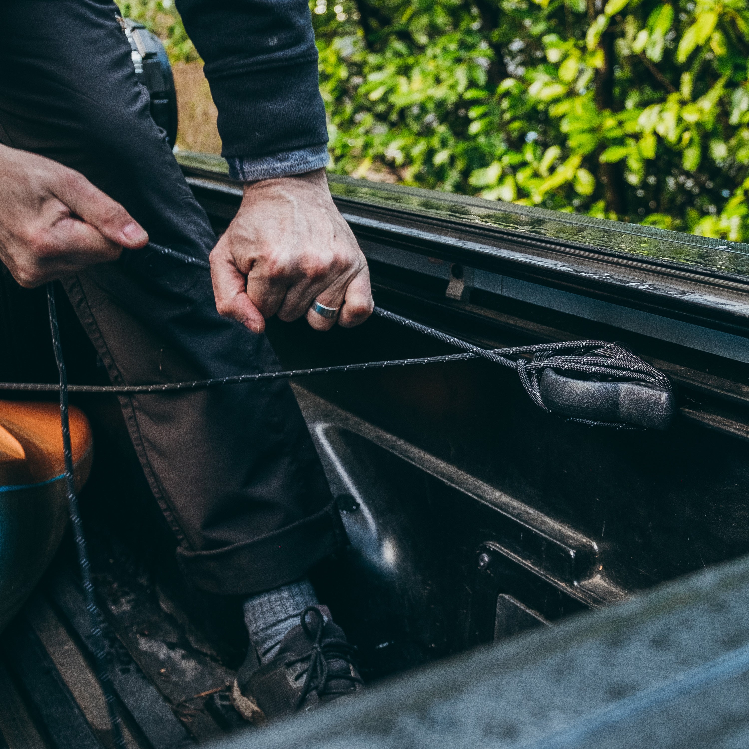 Hands wrapping Paracord in Black Reflective Color against tie down in a boat, green foliage in the background