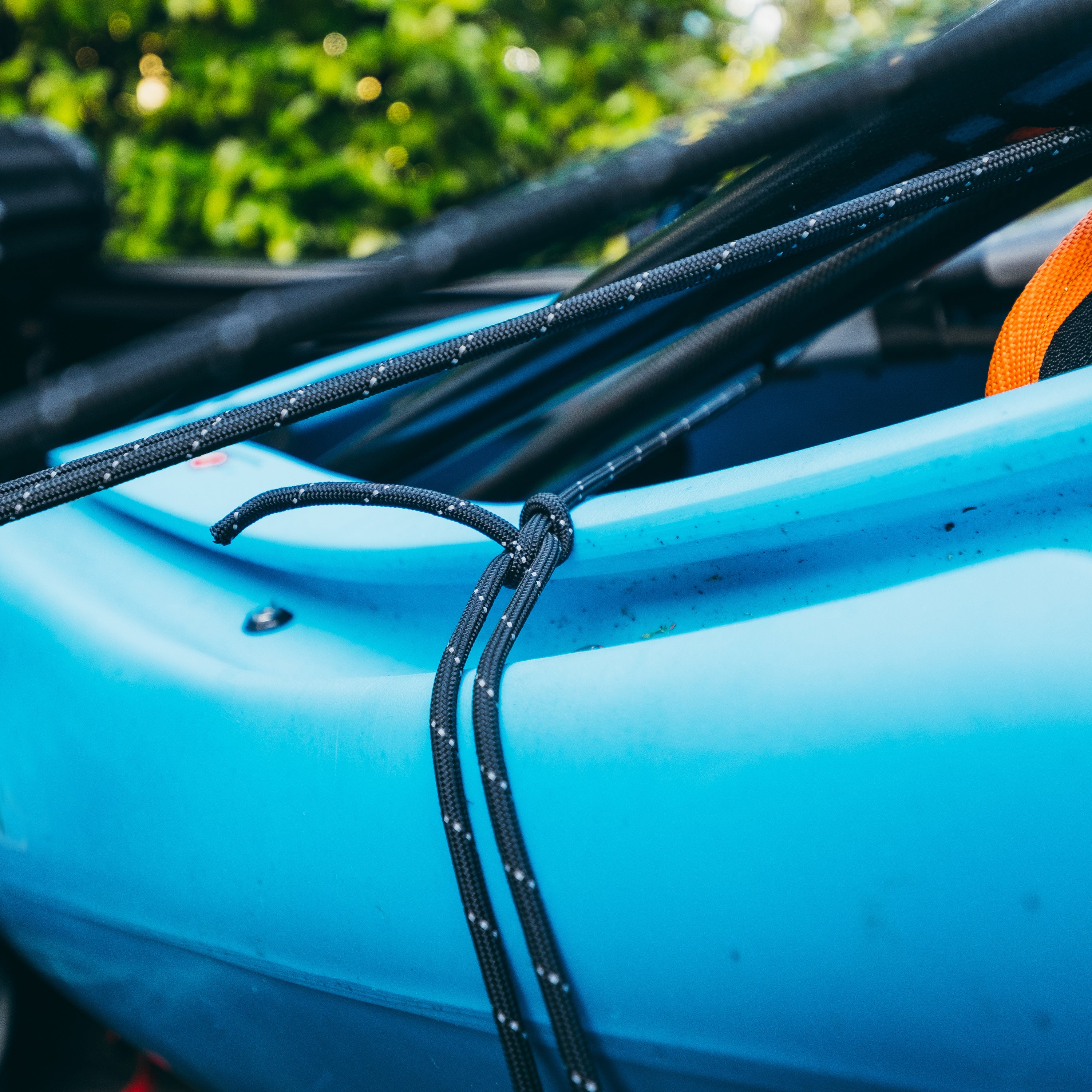 Paracord in Black Reflective Color tied around a blue kayak with green foliage in the background
