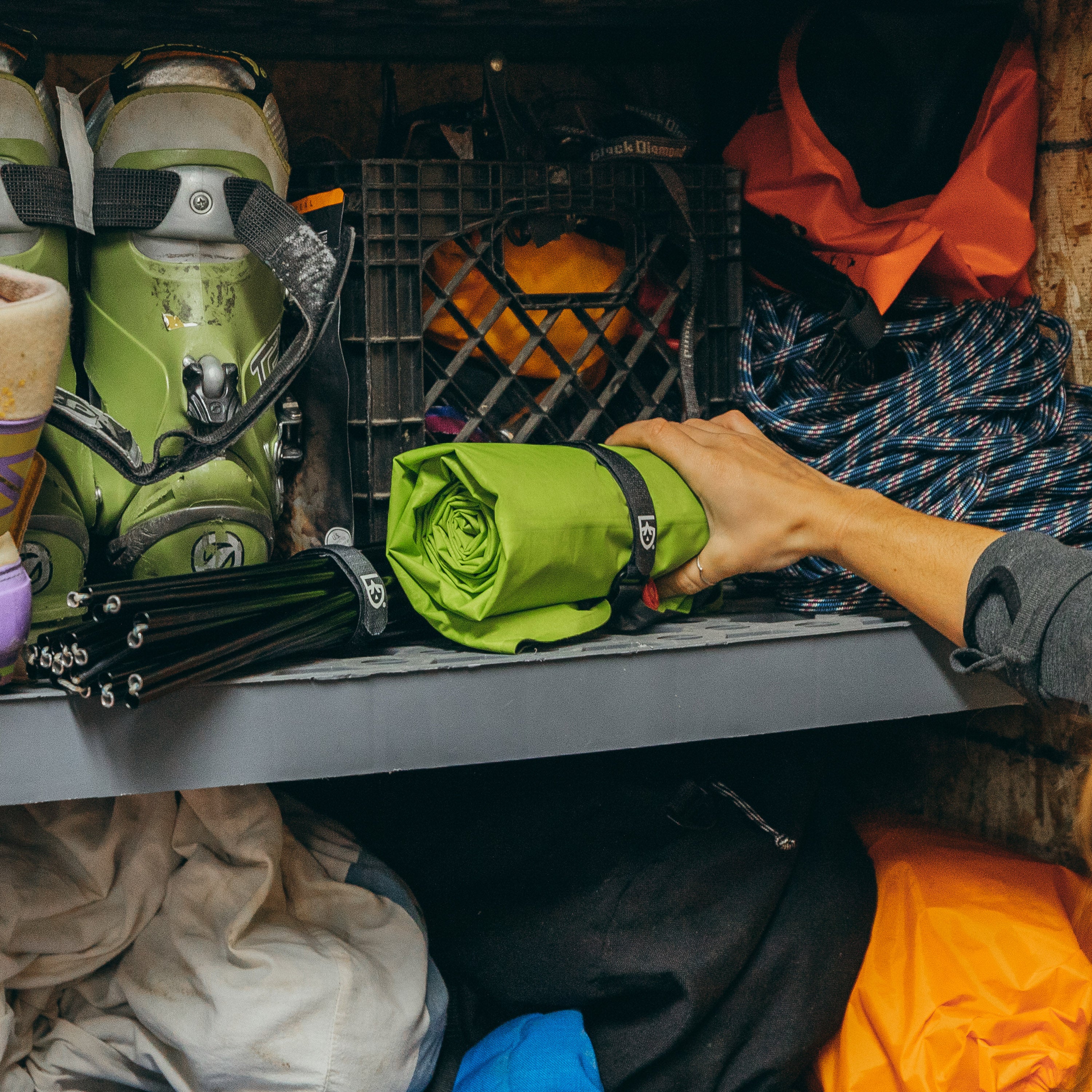Hands placing a rolled up inflatable camp chair held together with Fast Wrap on a gear storage shelf in a garage