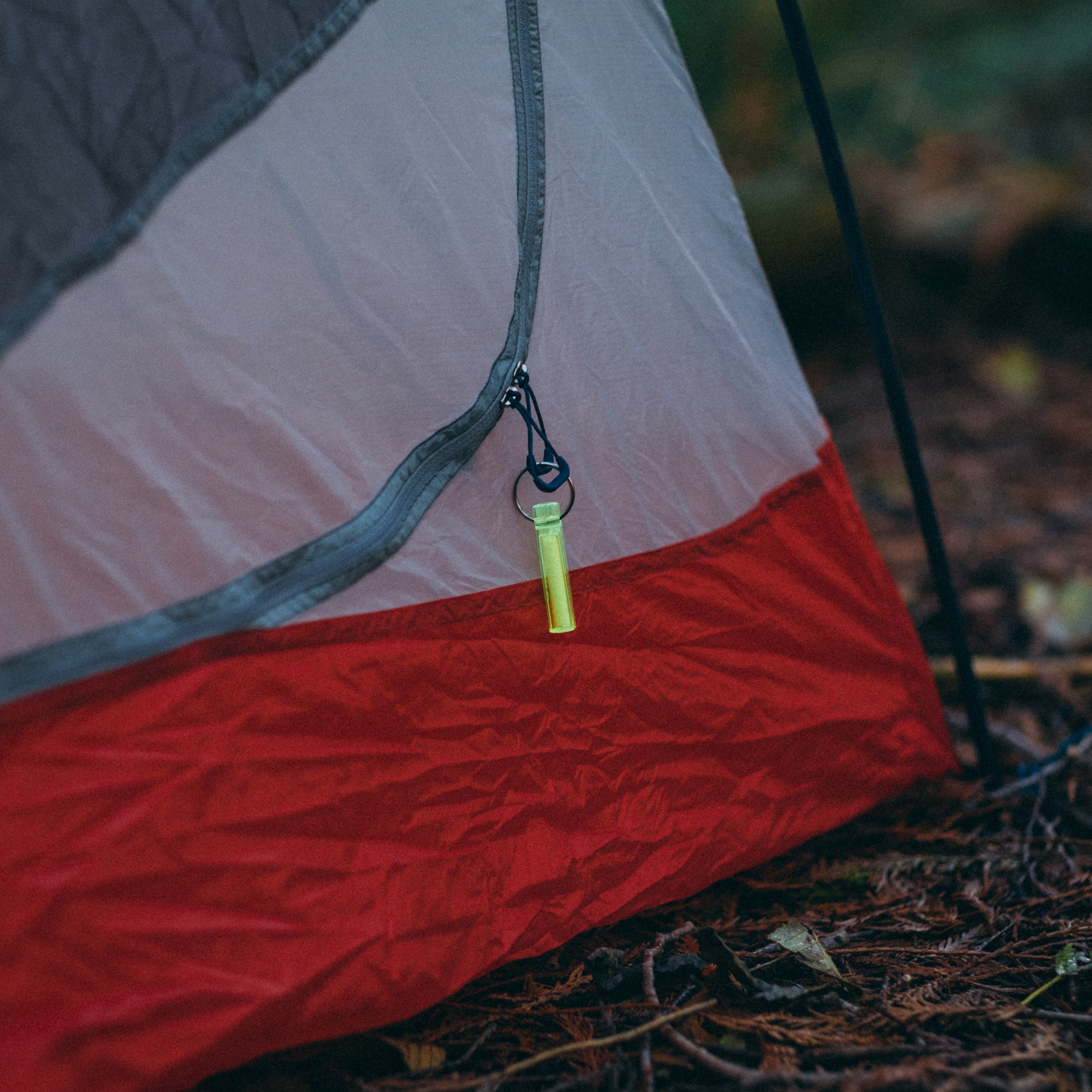 Ni Glo gear marker on the zipper of a red and white tent in the woods