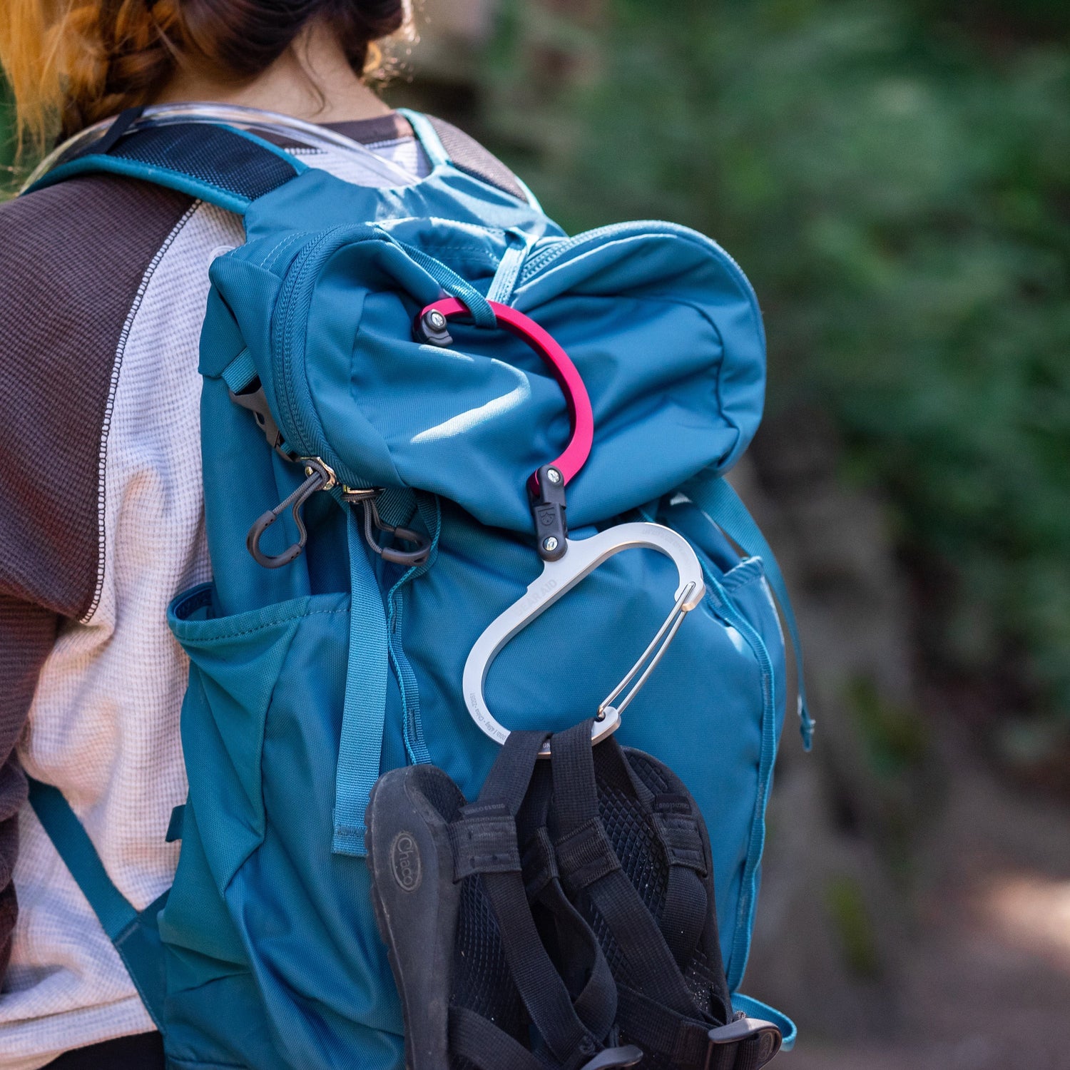 Heroclip open and hanging on a backpack of person hiking. Shoes are hanging from the heroclip.