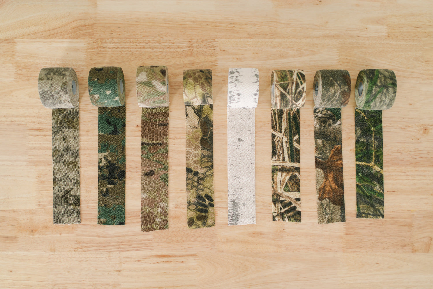 Line up of all GEAR AID Camo Form concealment wraps on wood table