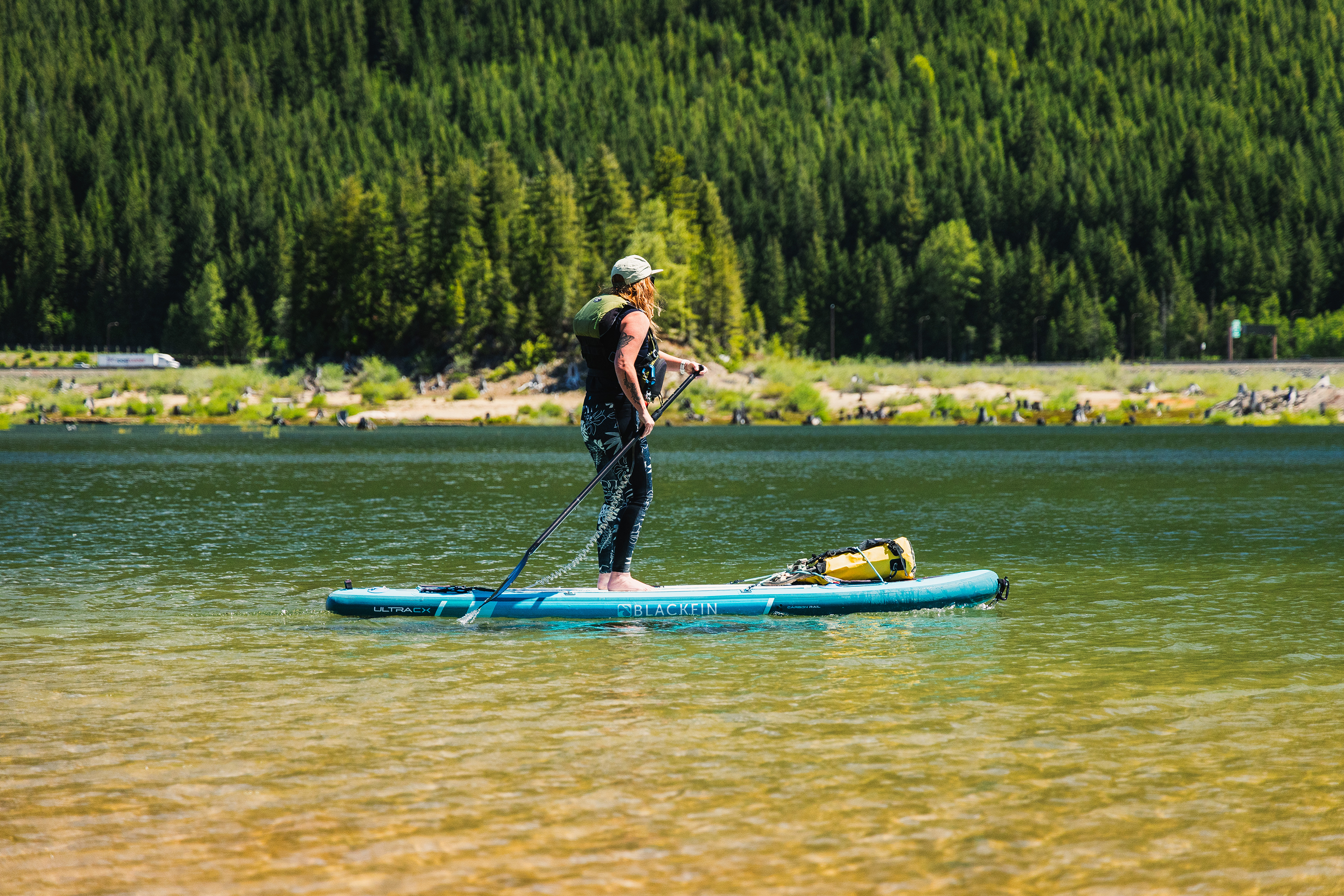 Person on blue paddle board in calm lake with shore and trees in background