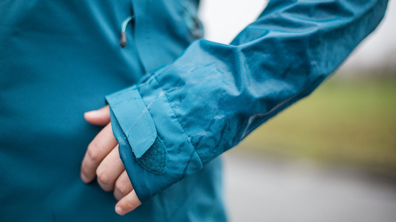 Hand and arm in blue GORE-TEX jacket, background is rainy and blurry