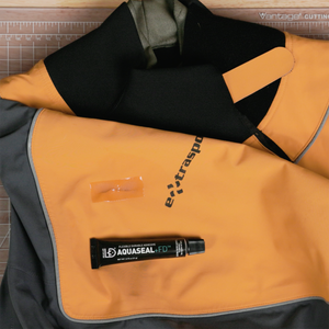 A small tube of Aquaseal FD sitting on a repaired orange, black, and gray drysuit top