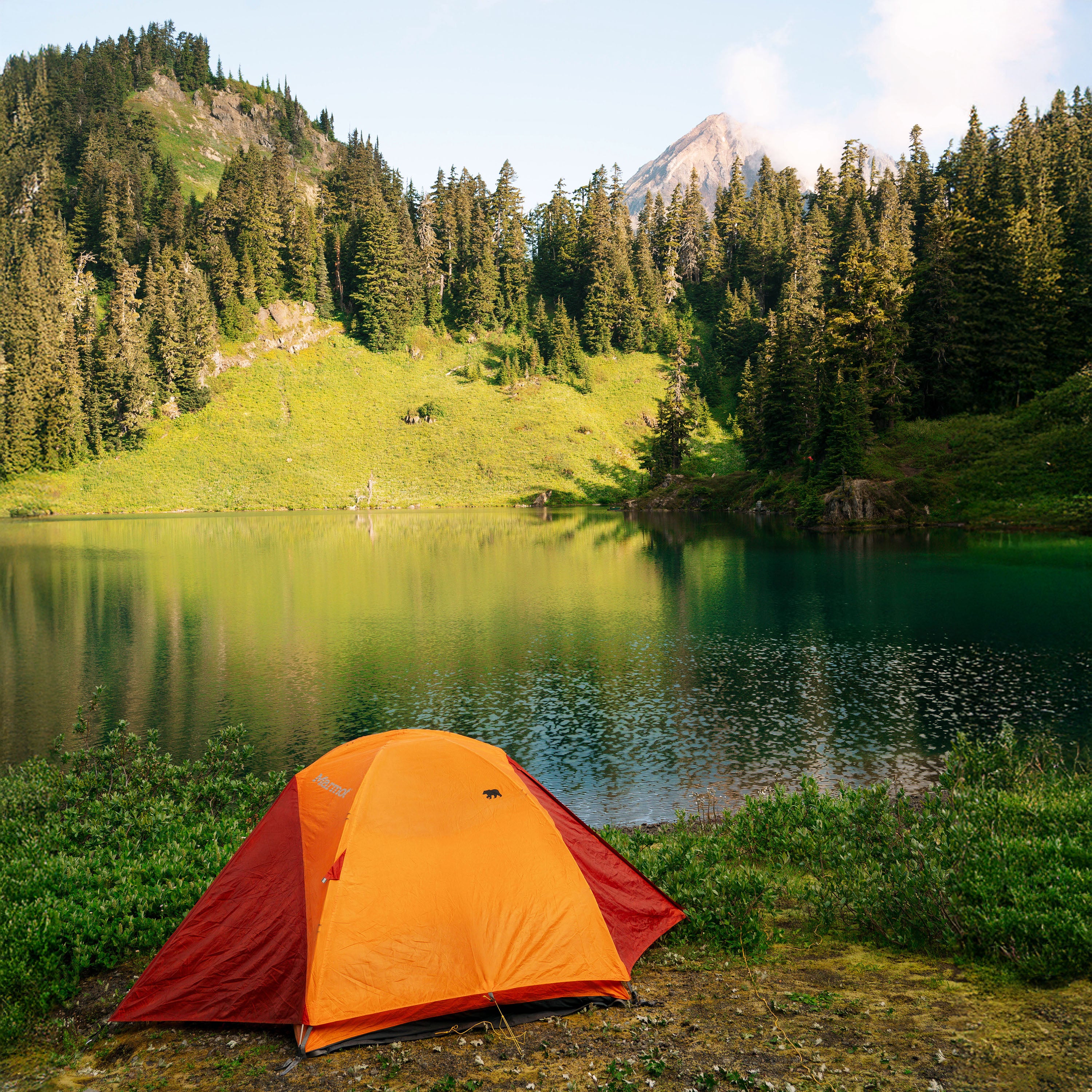 Orange and red tent set up by a lake with mountains in the background