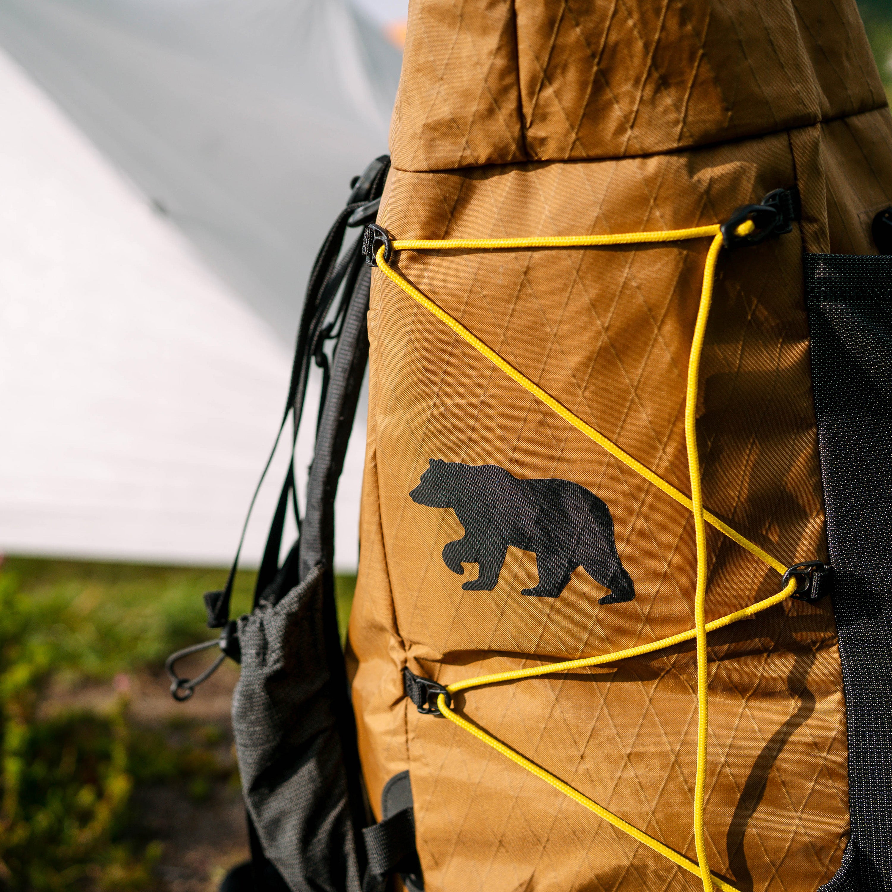 Brown backpack with bear repair patch and yellow straps in outdoor setting
