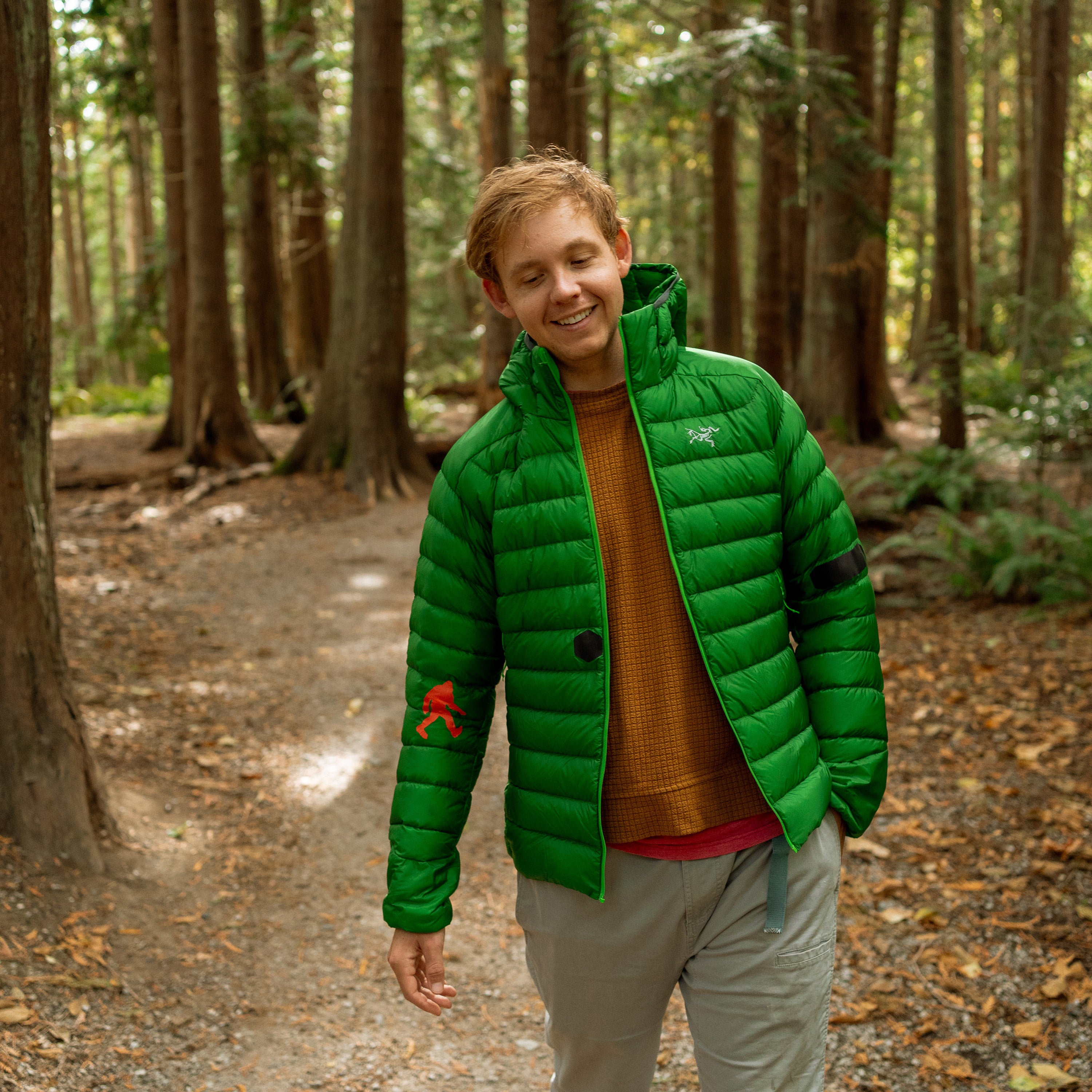 Person wearing a green puffer jacket in a forest setting, patches on jacket