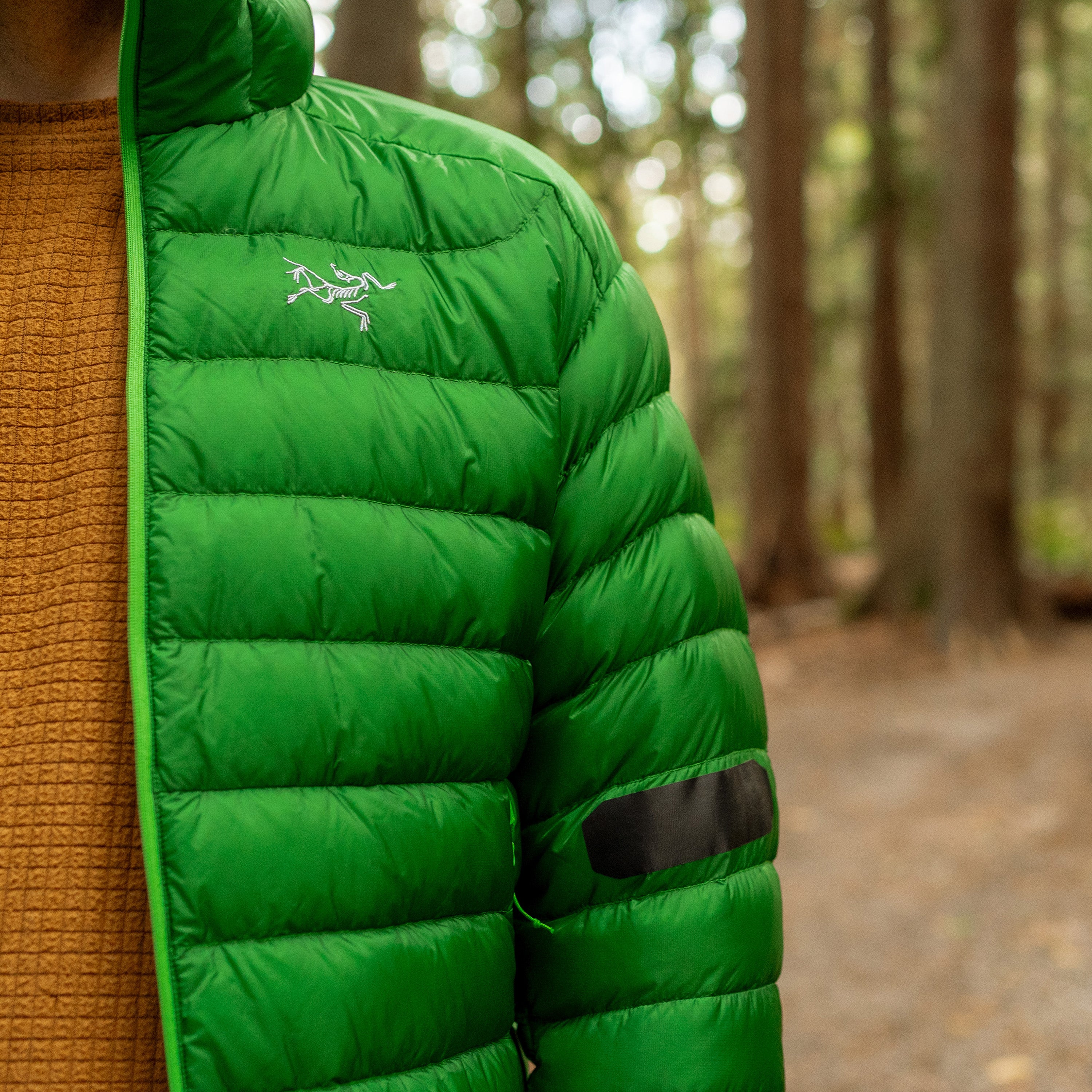 Green puffer jacket with a brand logo worn by a person in a forest setting