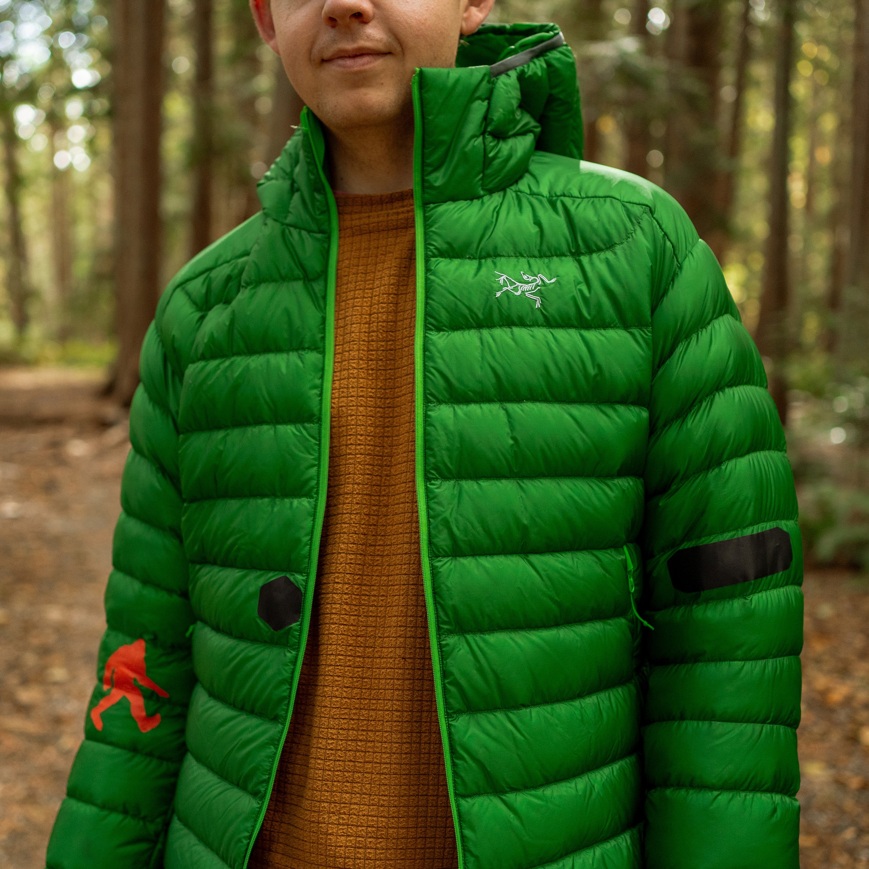 Person wearing a green puffer jacket with a brand logo in a forest setting