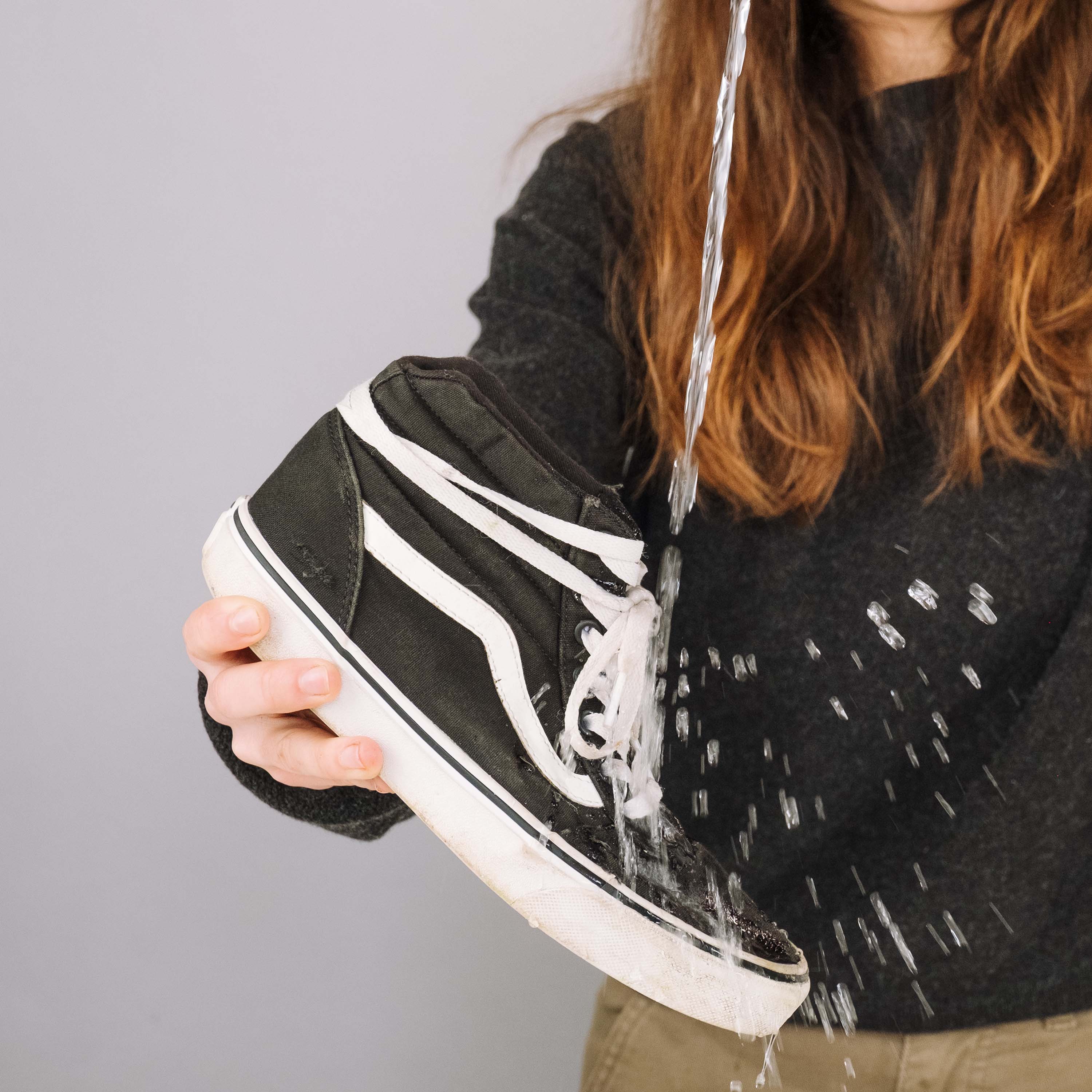 Person holding a black and white sneaker with water dripping from it against a gray background