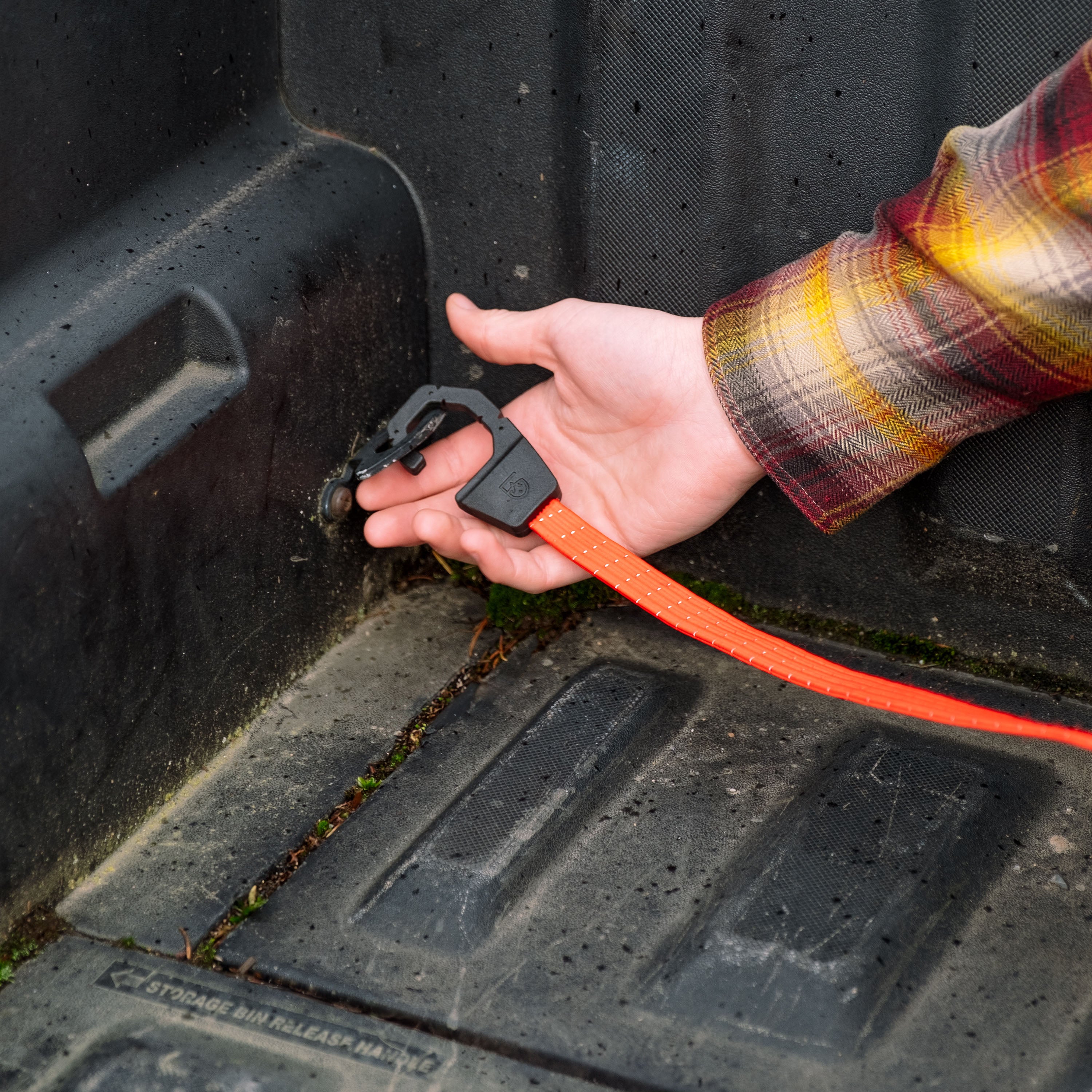 Person wearing a flannel and attaching a Holdfast Strap to a the bed of a pickup truck