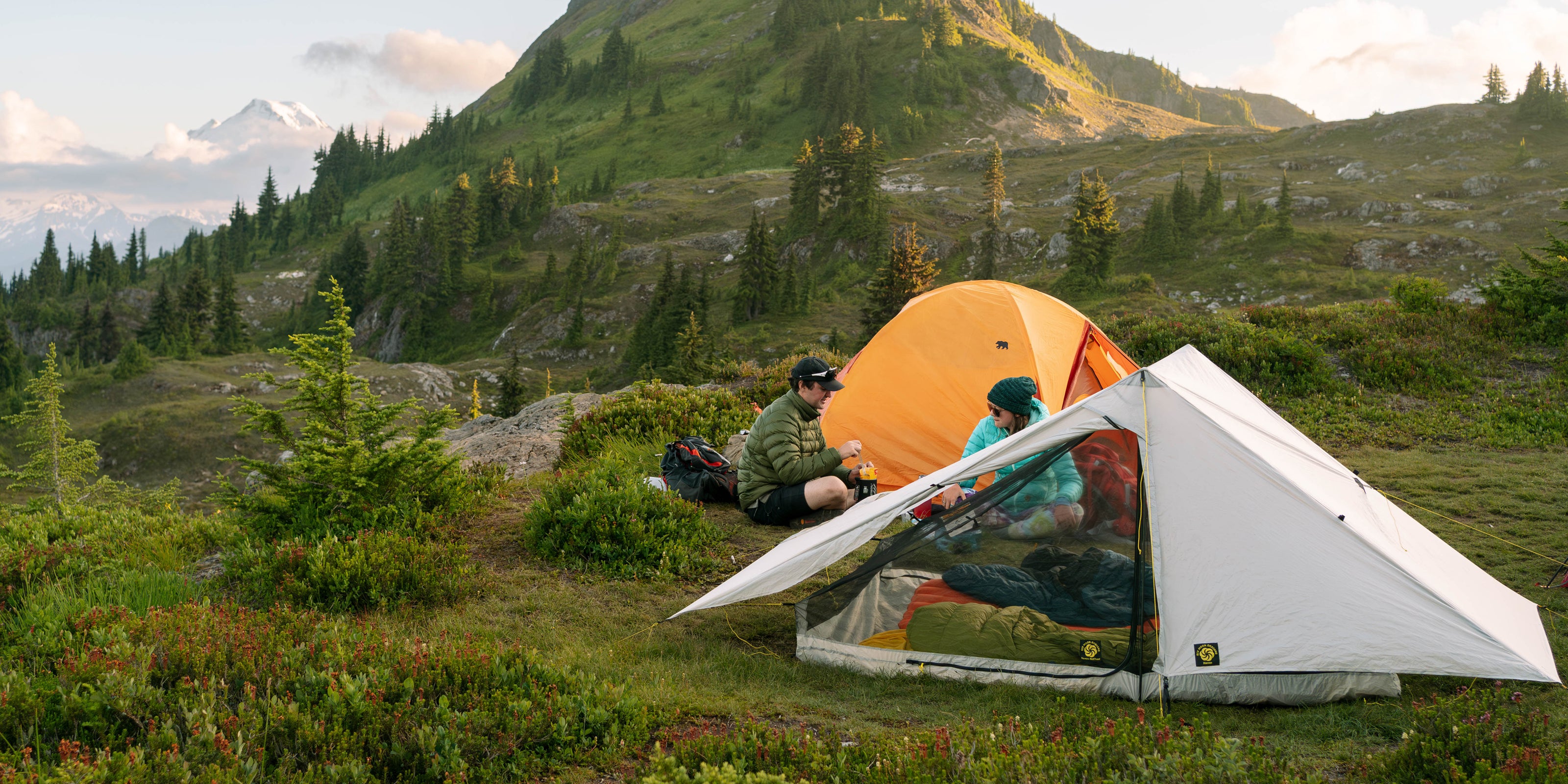 Two people camping in a scenic mountain area with two tents.